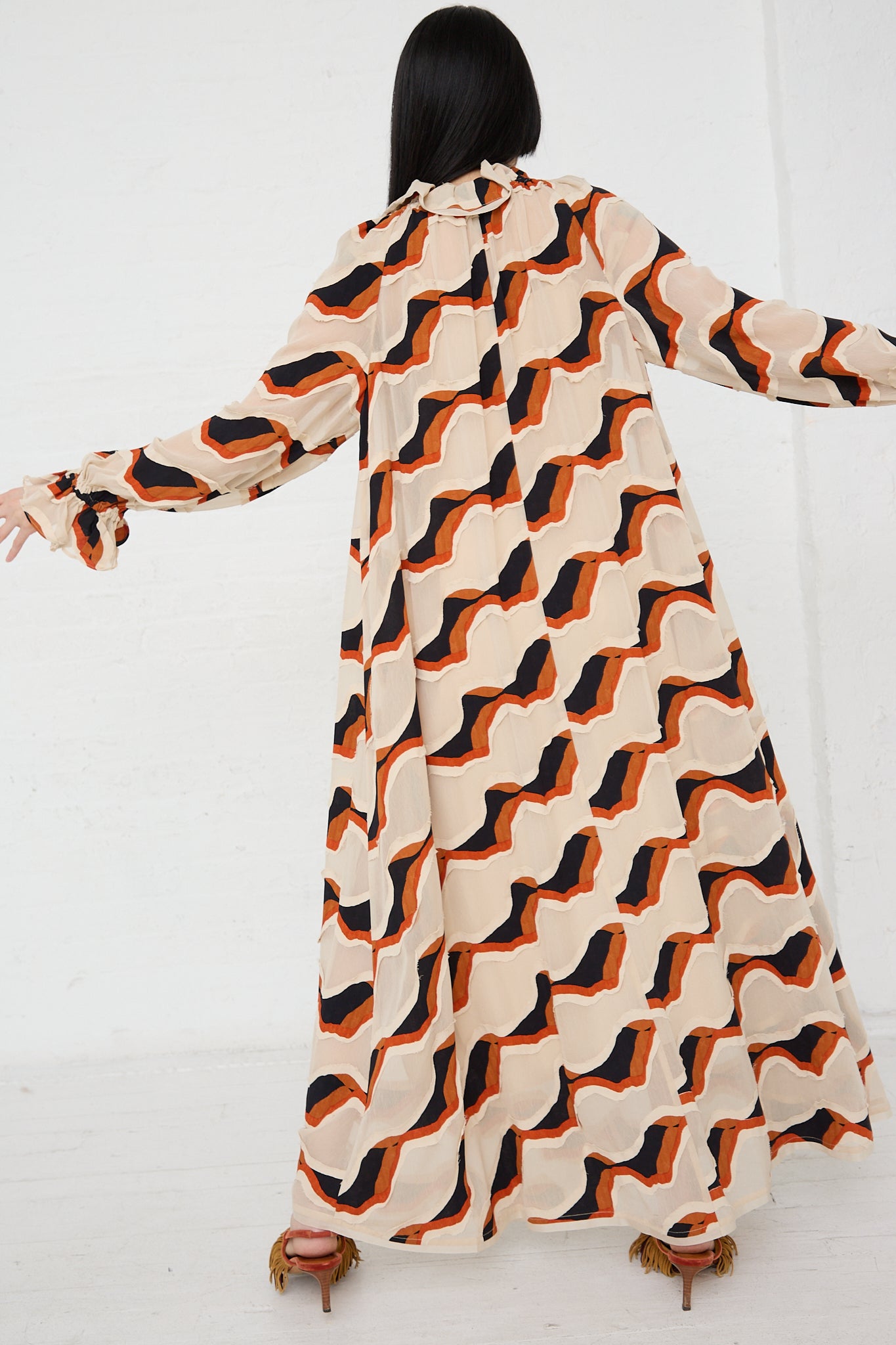 A woman wearing the Ulla Johnson Echo Dress in Conch, a maxi dress in an orange and black print, waving stripe devore.