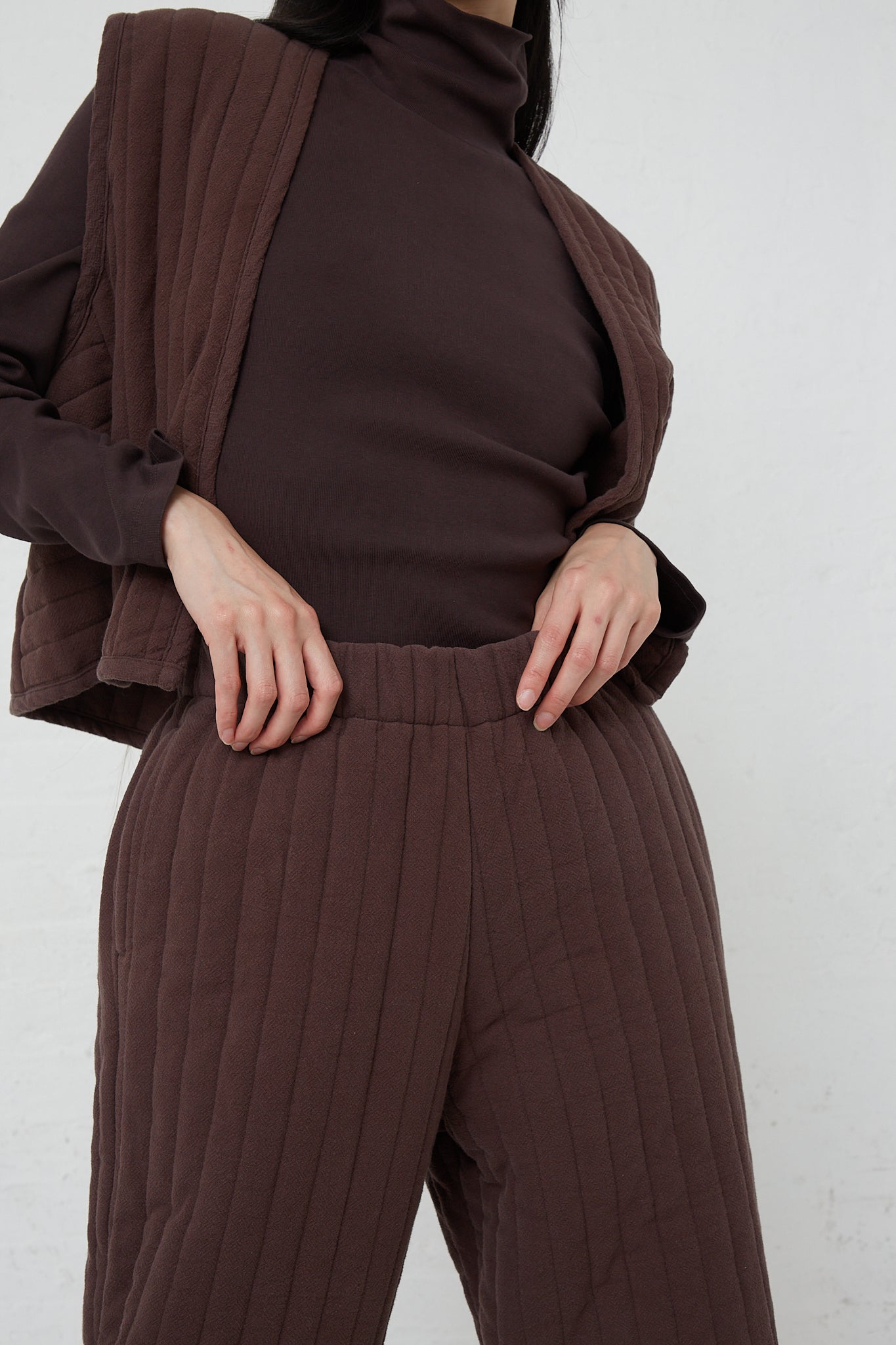A woman wearing a turtle neck sweater and Black Crane's Quilted Easy Pants in Plum.