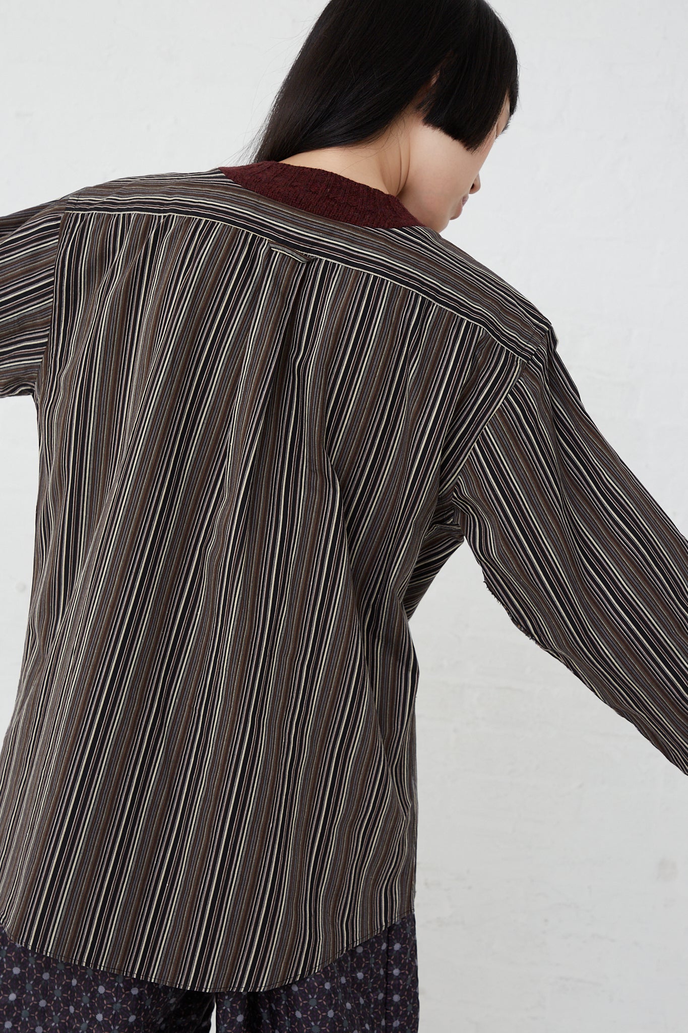 The back of a woman wearing a Bless No. 68 Front Insert Pullover in Stripe in a burgundy striped shirt.