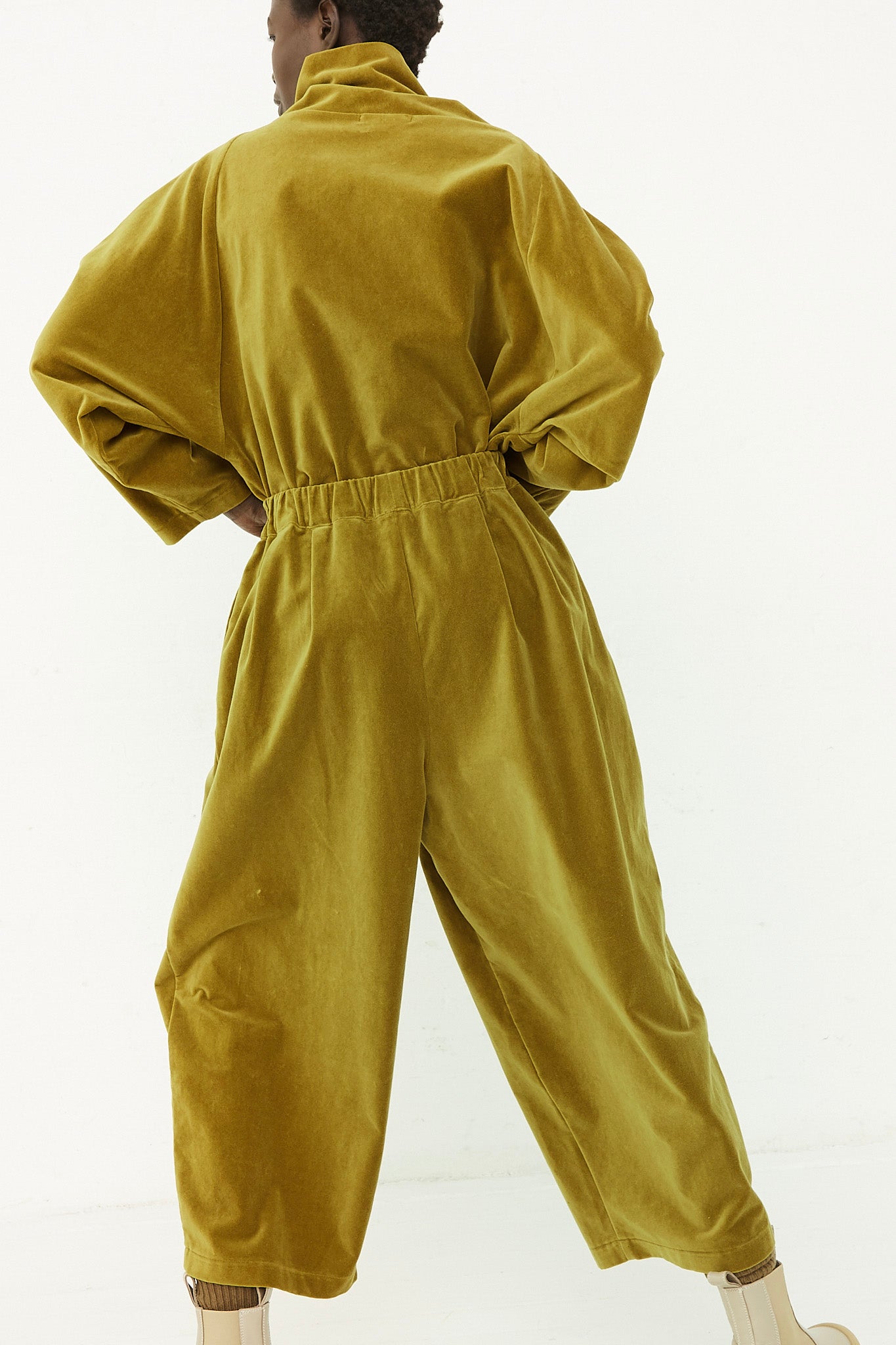 A woman is standing in a Black Crane Cotton Velveteen Wide Pants, olive jumpsuit with an elasticated waist.
