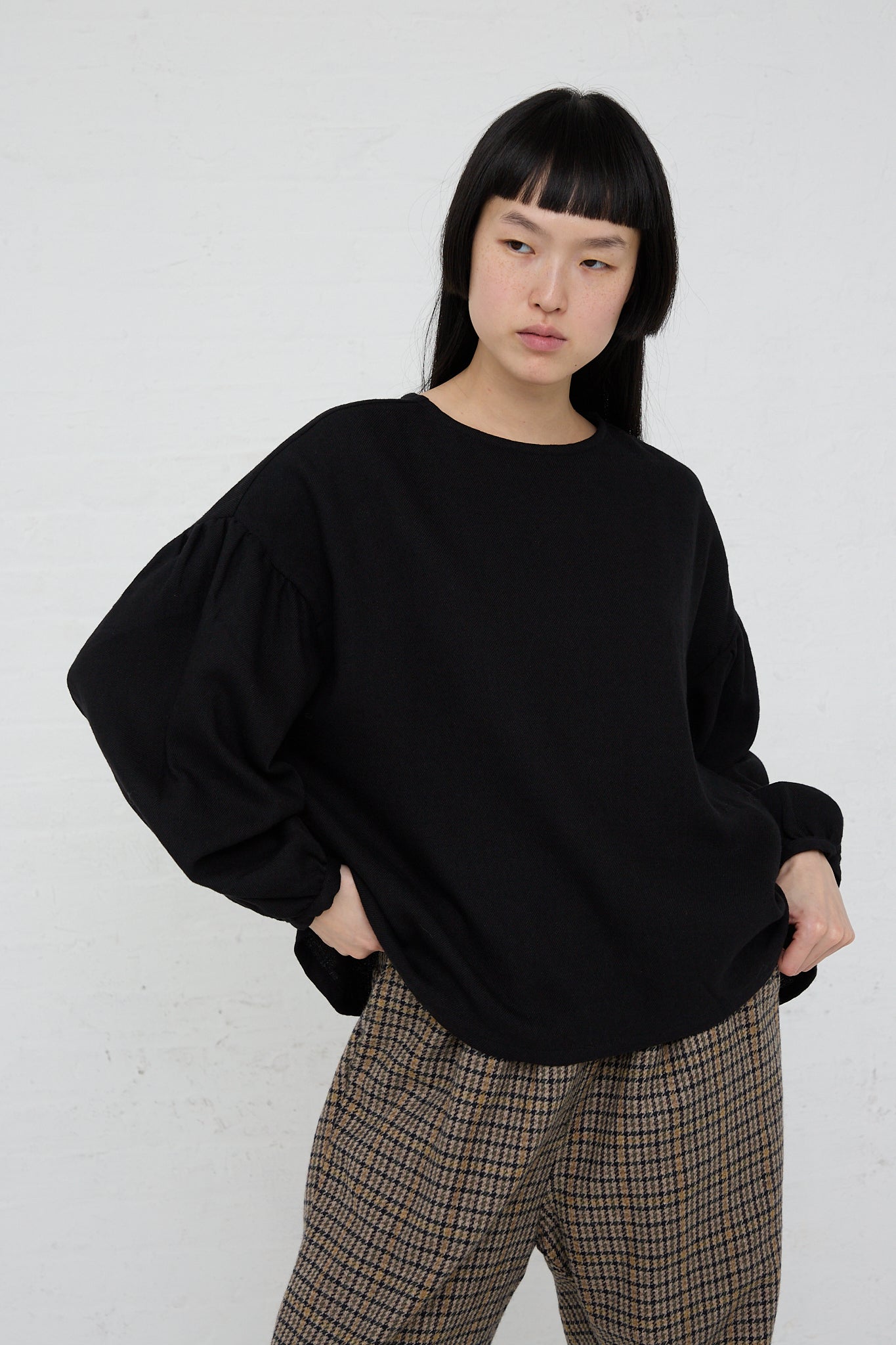 A woman wearing a relaxed fit Two-Way Blouse in Black from Ichi and plaid pants.
