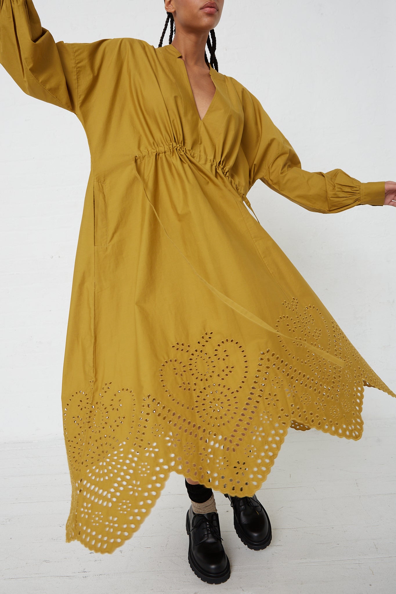 A woman wearing a Rachel Comey Bridge Dress with Hearts Eyelet in Chartreuse with a drawstring tie waist, paired with black boots.