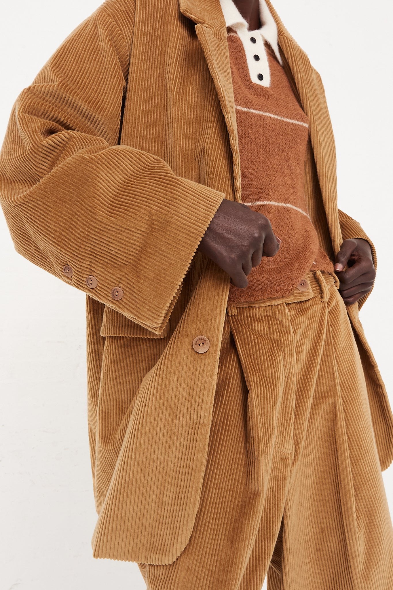 A model wearing a button blazer in a cotton corduroy featuring a notched collar, two flap pockets in front, and back vent. Blazer open highlighting knit and pants. Up close view of corduroy details. Oversized fit. Designed by Cordera - Oroboro Store
