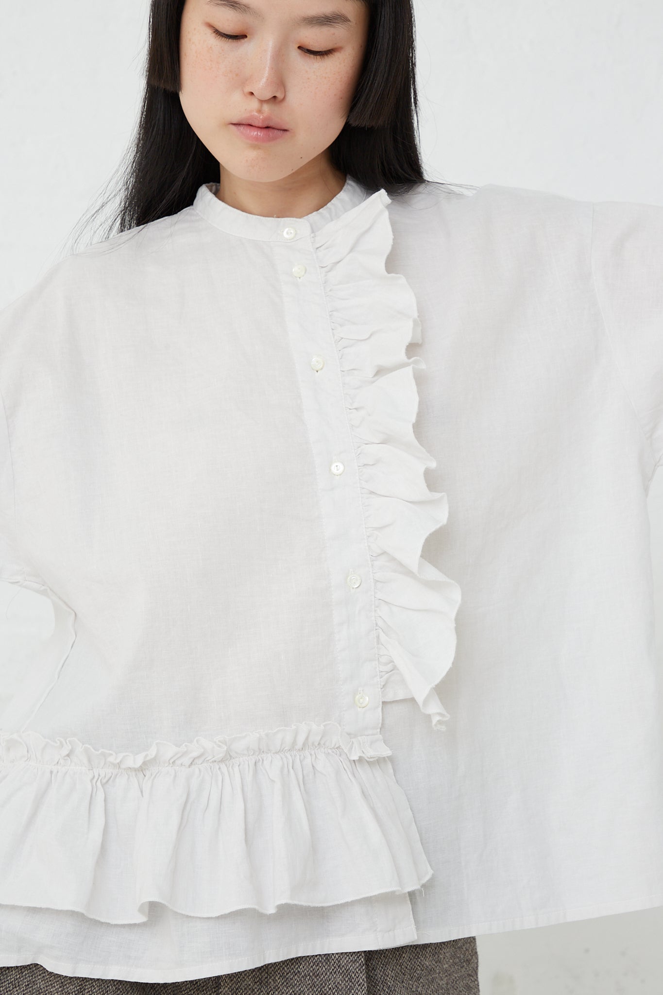 A woman wearing a nest Robe UpcycleLino Linen Gathered Frill Blouse in Off White with a front button closure.