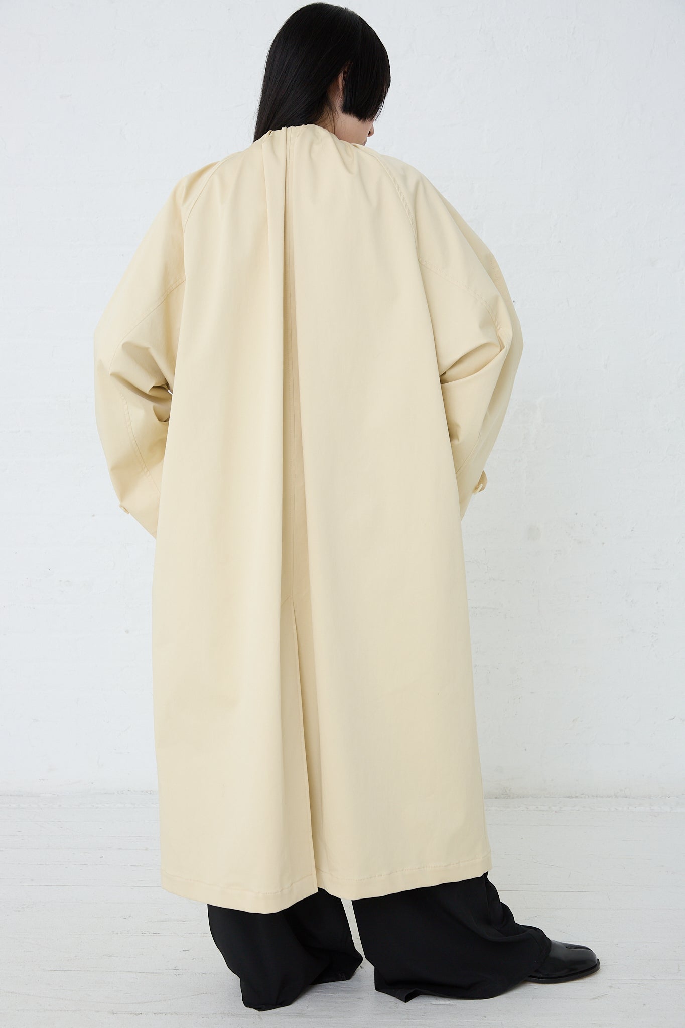 A person in an MM6 Pale Yellow Trench Coat. Back view and full length.