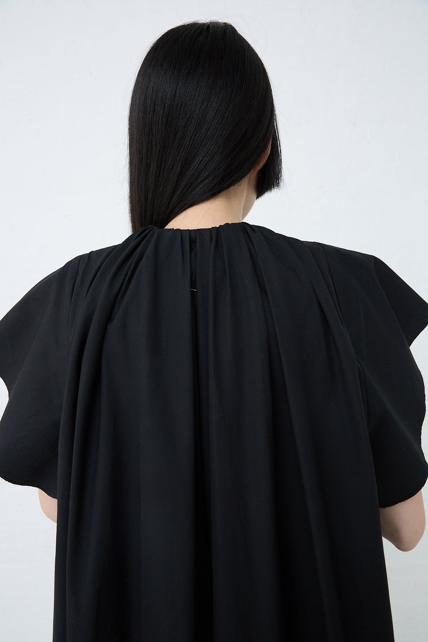 The back view of a woman wearing an MM6 Maxi Dress in Black. Up close view.