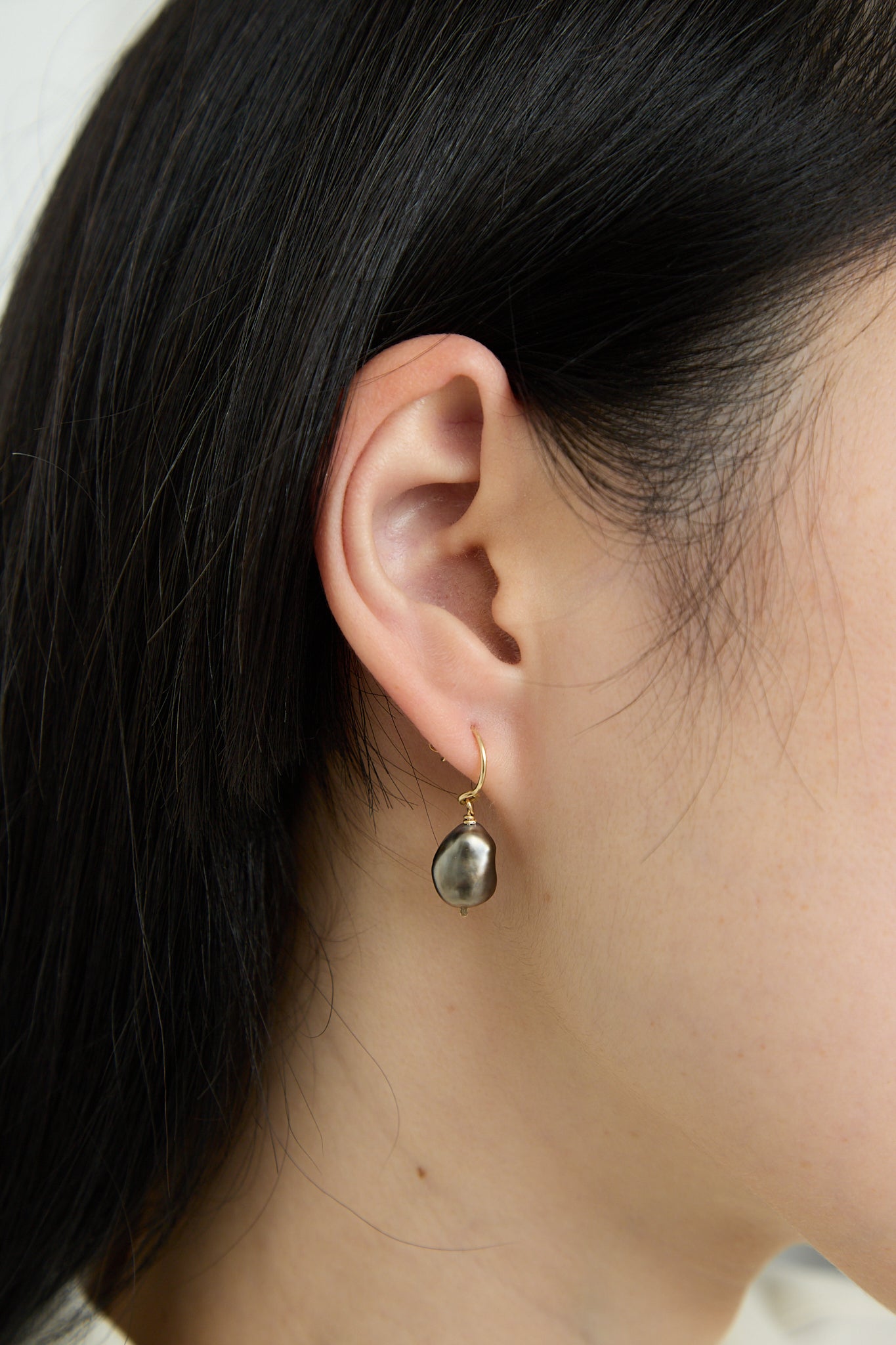A woman wearing a 14K Crescent Charm Earrings in Grey Keshi Pearl with a black stone dangling from it, made by Mary MacGill. Side view on model. Up close.