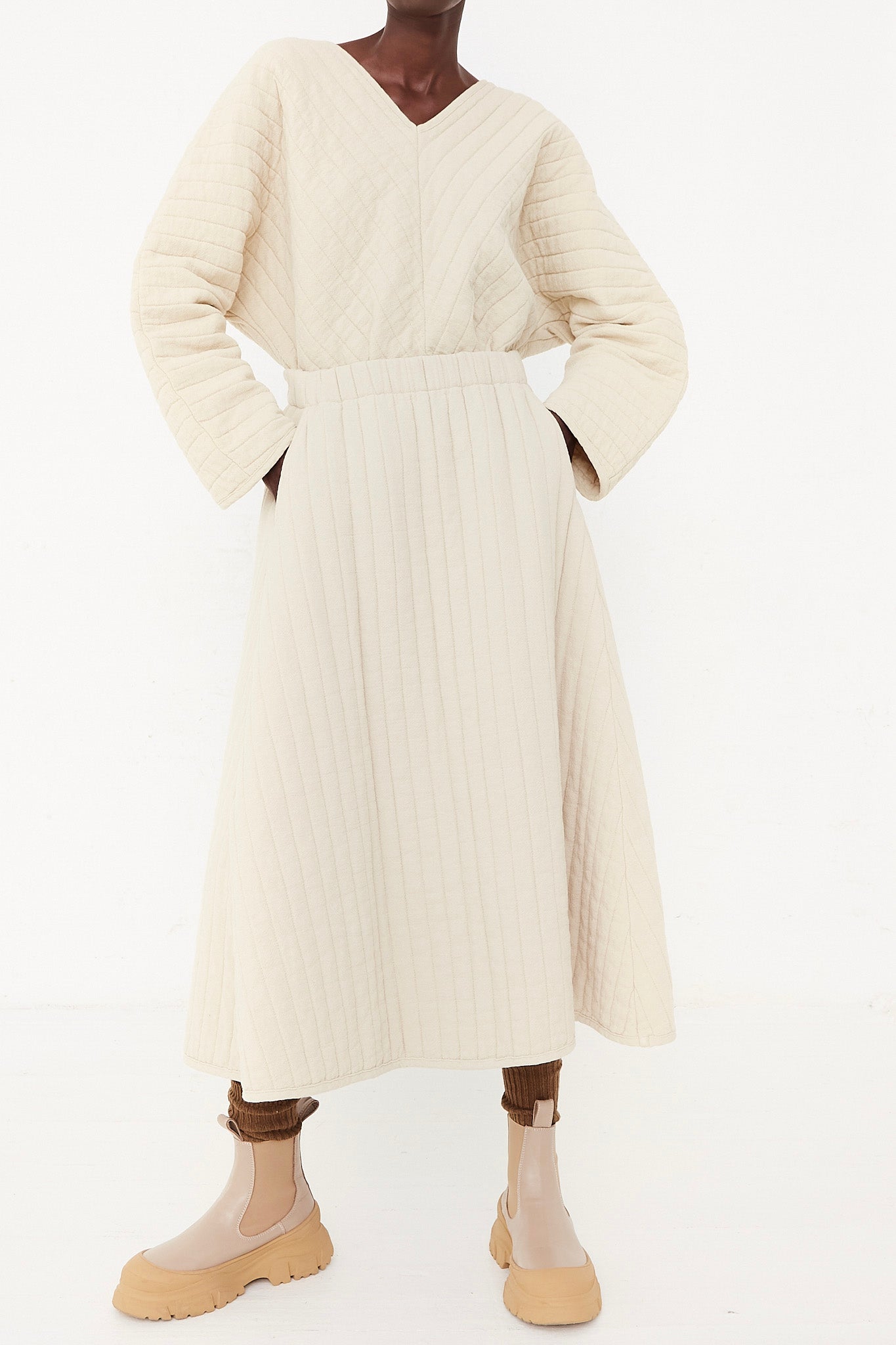 The model is wearing a quilted skirt in ivory paired with tan boots.
