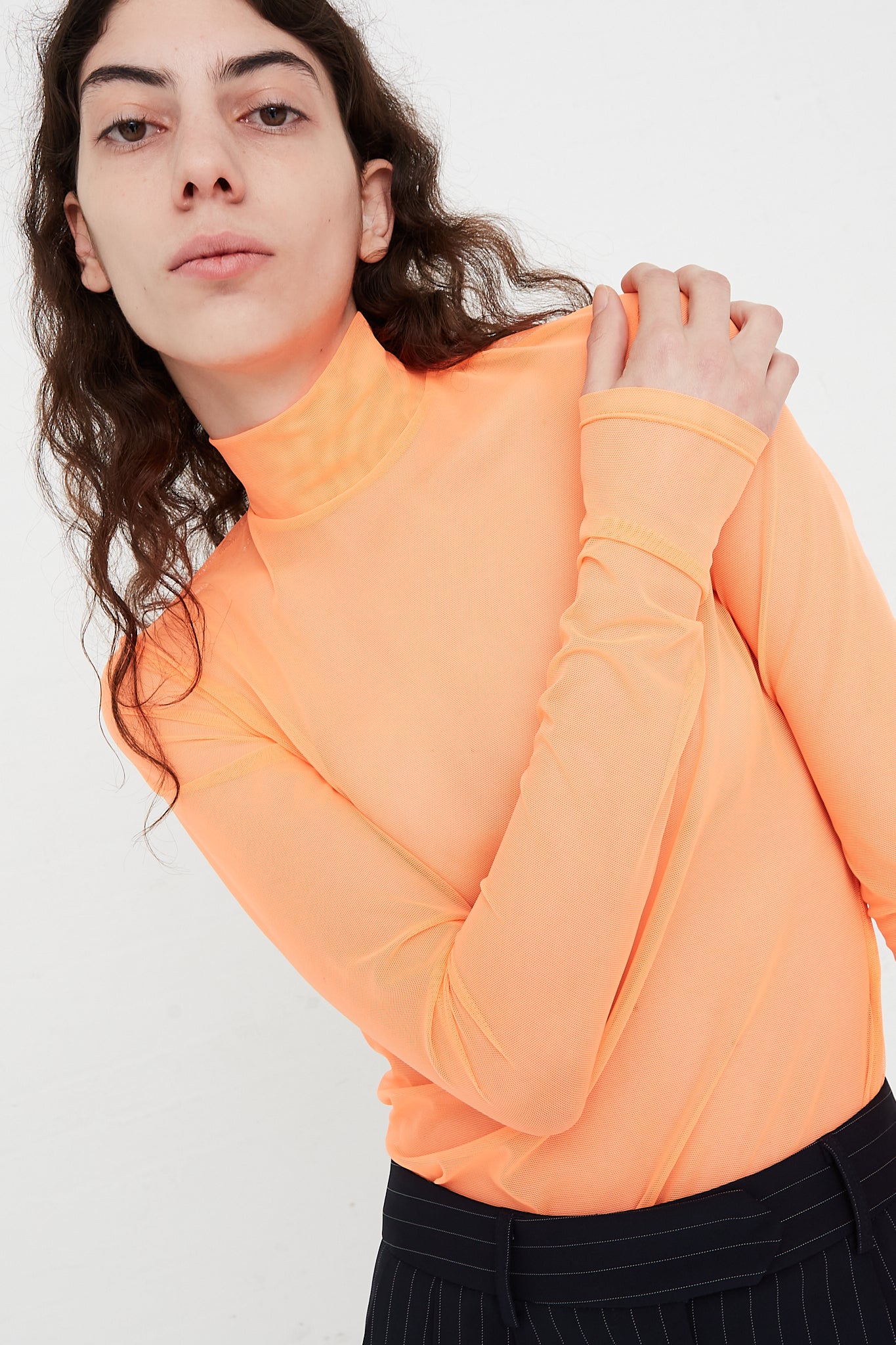 A model wearing a Long Sleeve Mesh Mockneck in Fluoro Orange designed by NOMIA brand.
