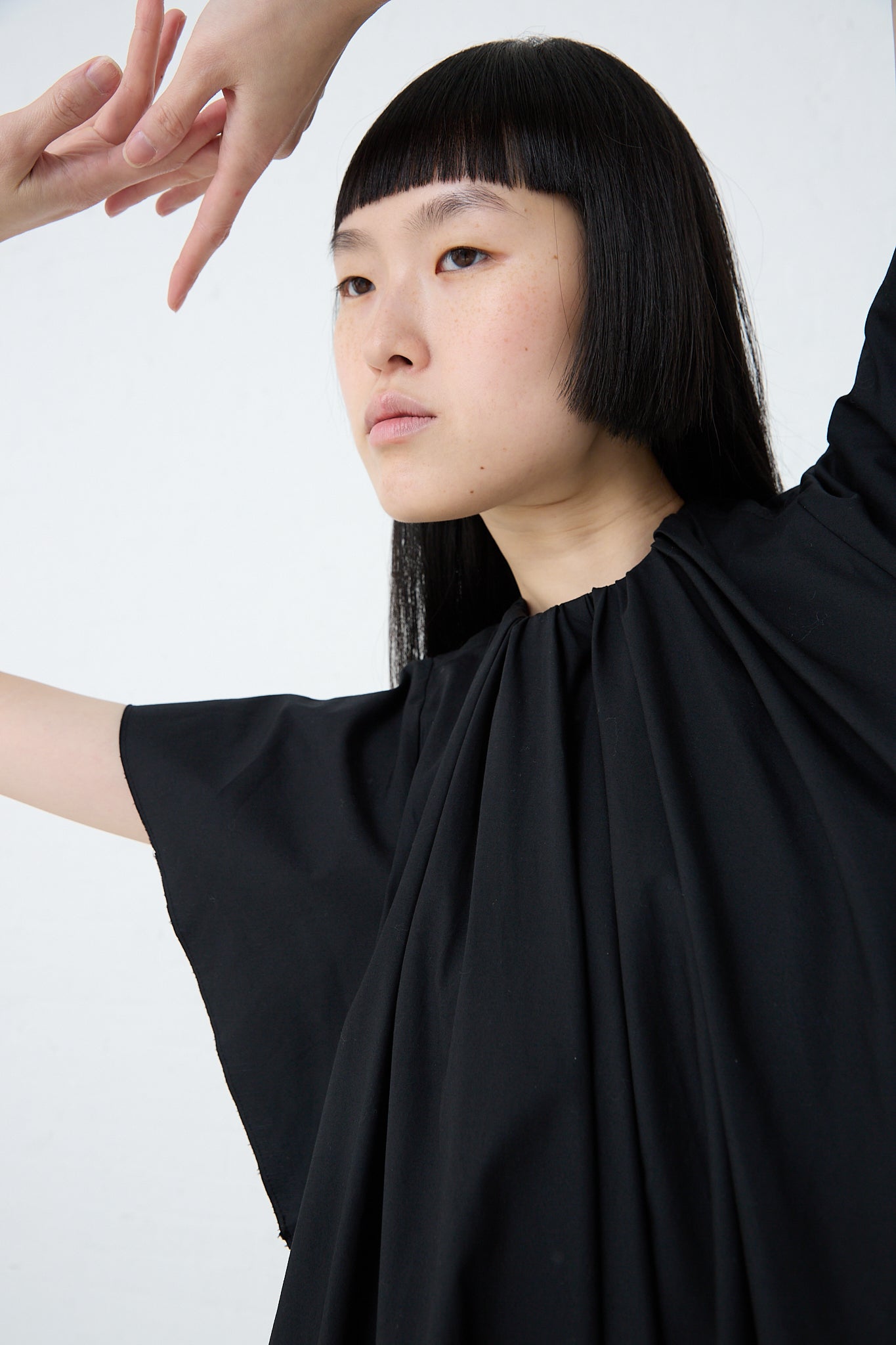 A woman wearing an MM6 Maxi Dress in Black with ruffled sleeves made from cotton poplin. Up close view. Model's arms are raised above head.