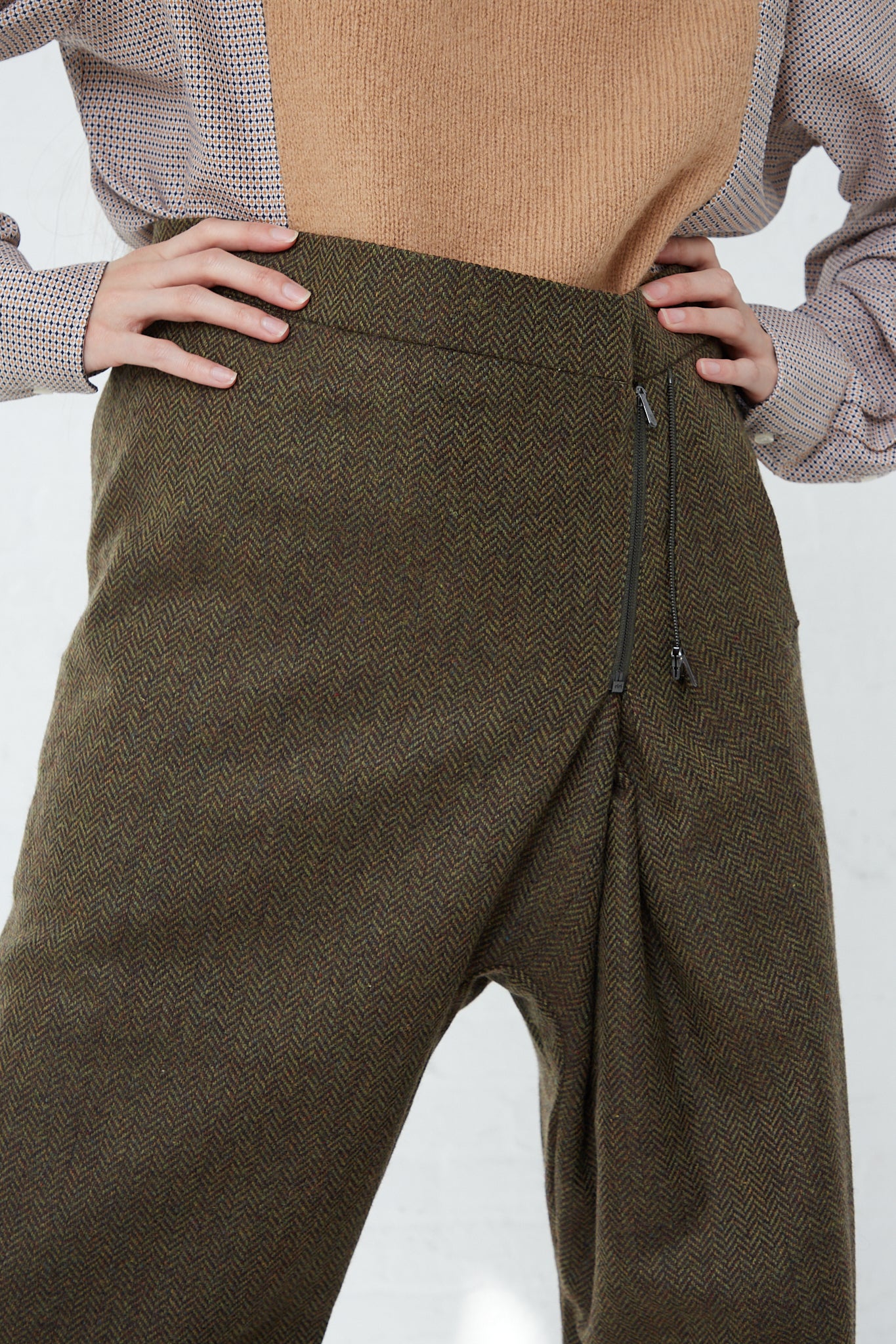 A woman wearing the Bless No. 75 Wool Long Pant in Purple Greenish Tweed, a tan sweater with an adjustable zipper accent in front.