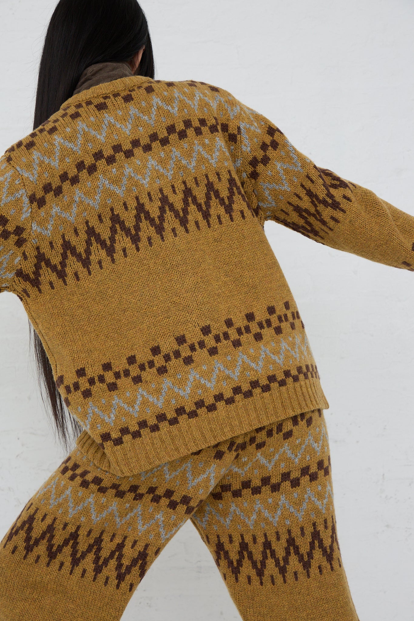 The back view of a woman wearing an Ichi Wool Knit Cardigan in Camel and pants.