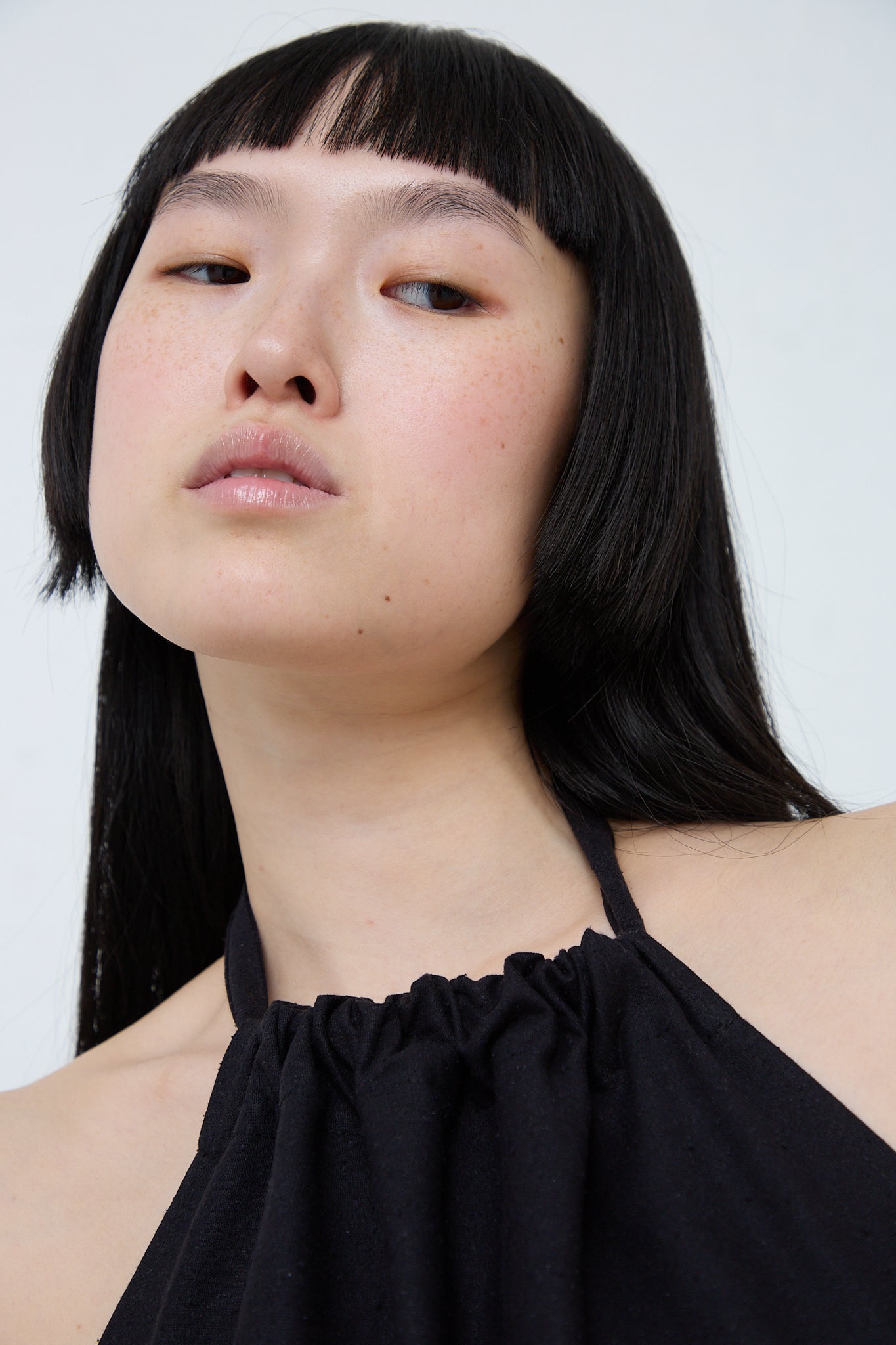 A sustainably produced Wild Silk Trope Apron Dress in Black by Baserange, with bangs and a black top made of black wild silk. Front view and up close of collar details.