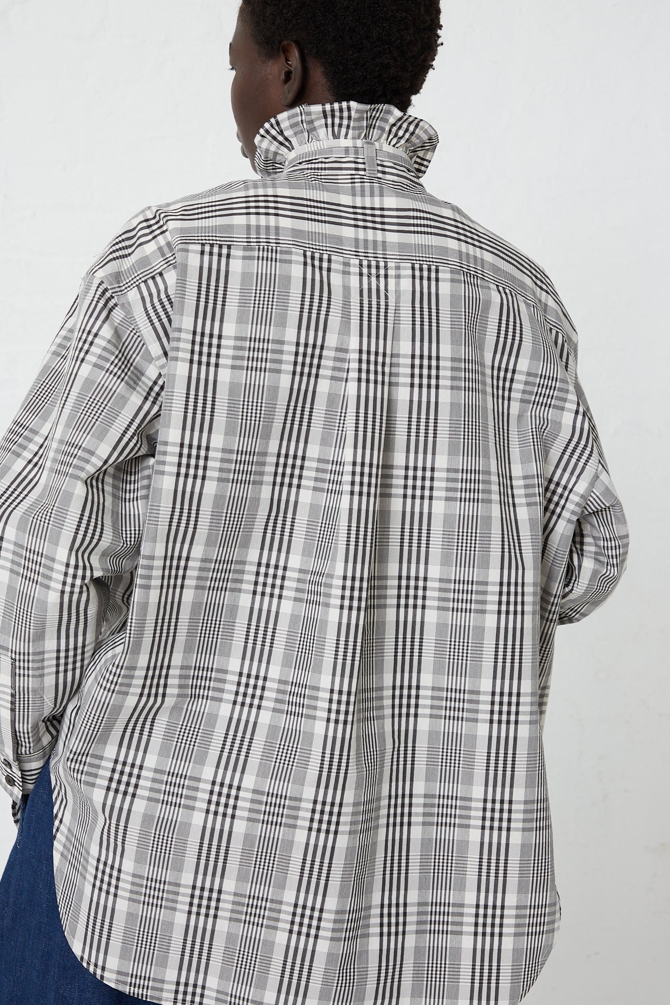 The back view of a woman wearing a KasMaria Poplin Tie Shirt with Ruffle Collar in Heavy Plaid.