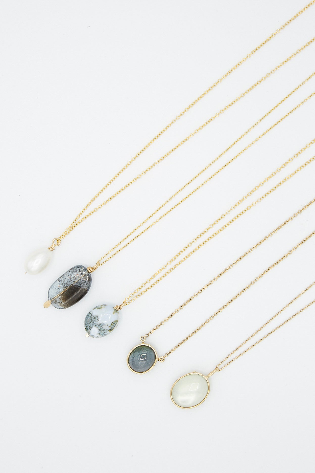 A group of Floating Necklaces in Light Green Tourmaline stones and pearls on a white background by Mary MacGill.