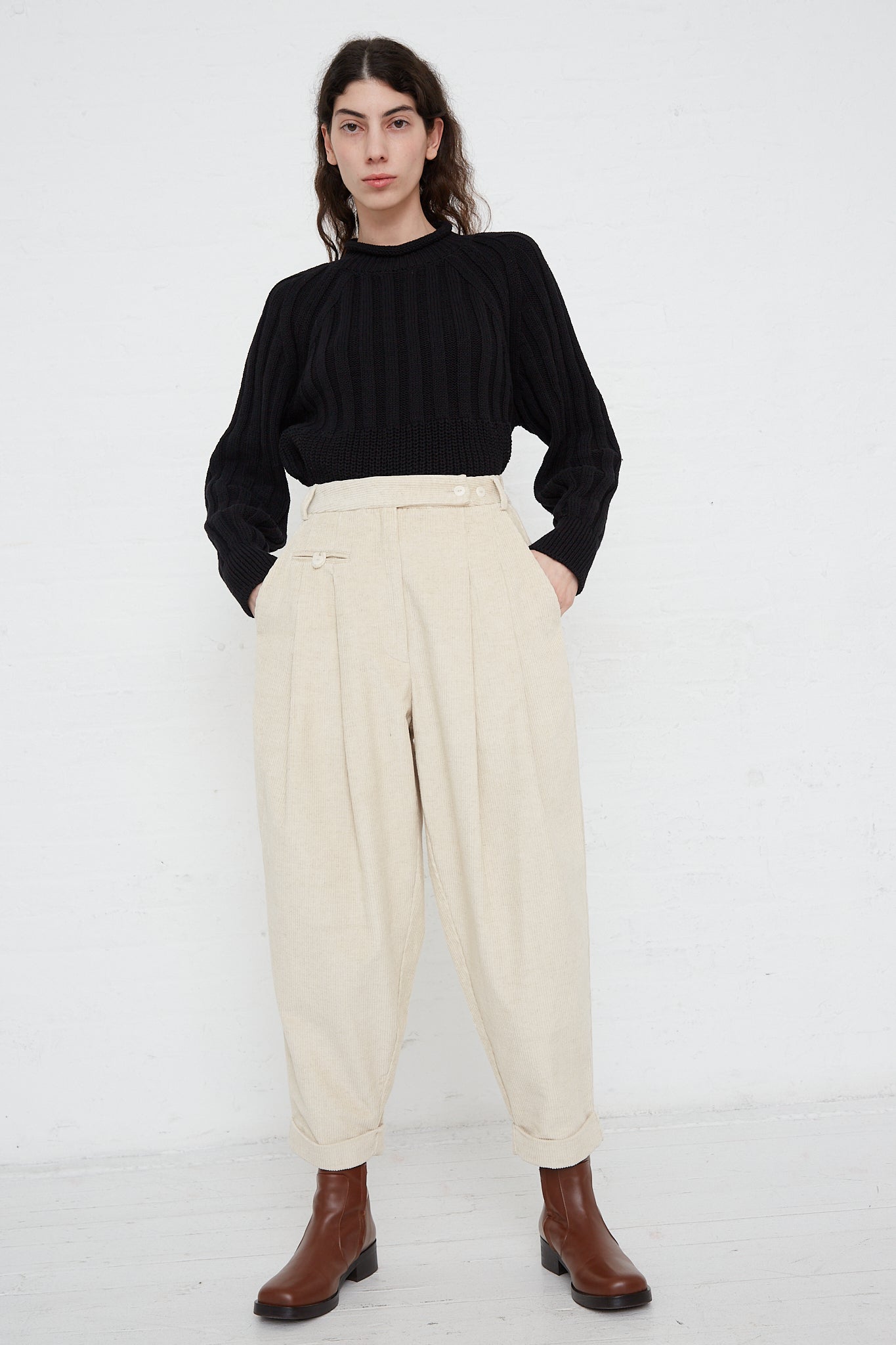 The model is wearing a black sweater and beige trousers made by Cordera. Front view. Full length.