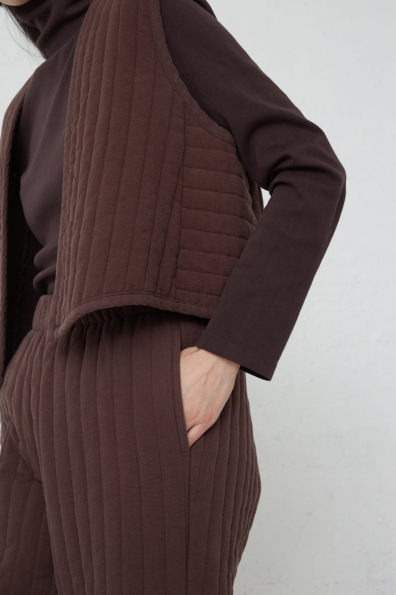 A woman wearing a brown quilted vest and Black Crane Quilted Easy Pants in Plum made of woven cotton.