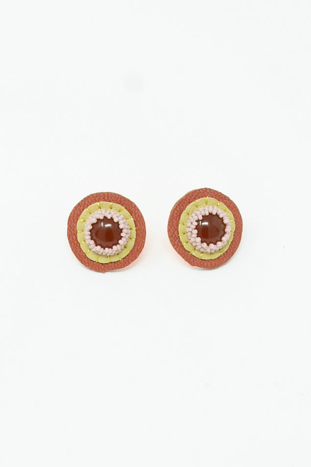 A pair of Carnelian Red stud earrings by Robin Mollicone on a white surface, crafted with hand-stitched leather.