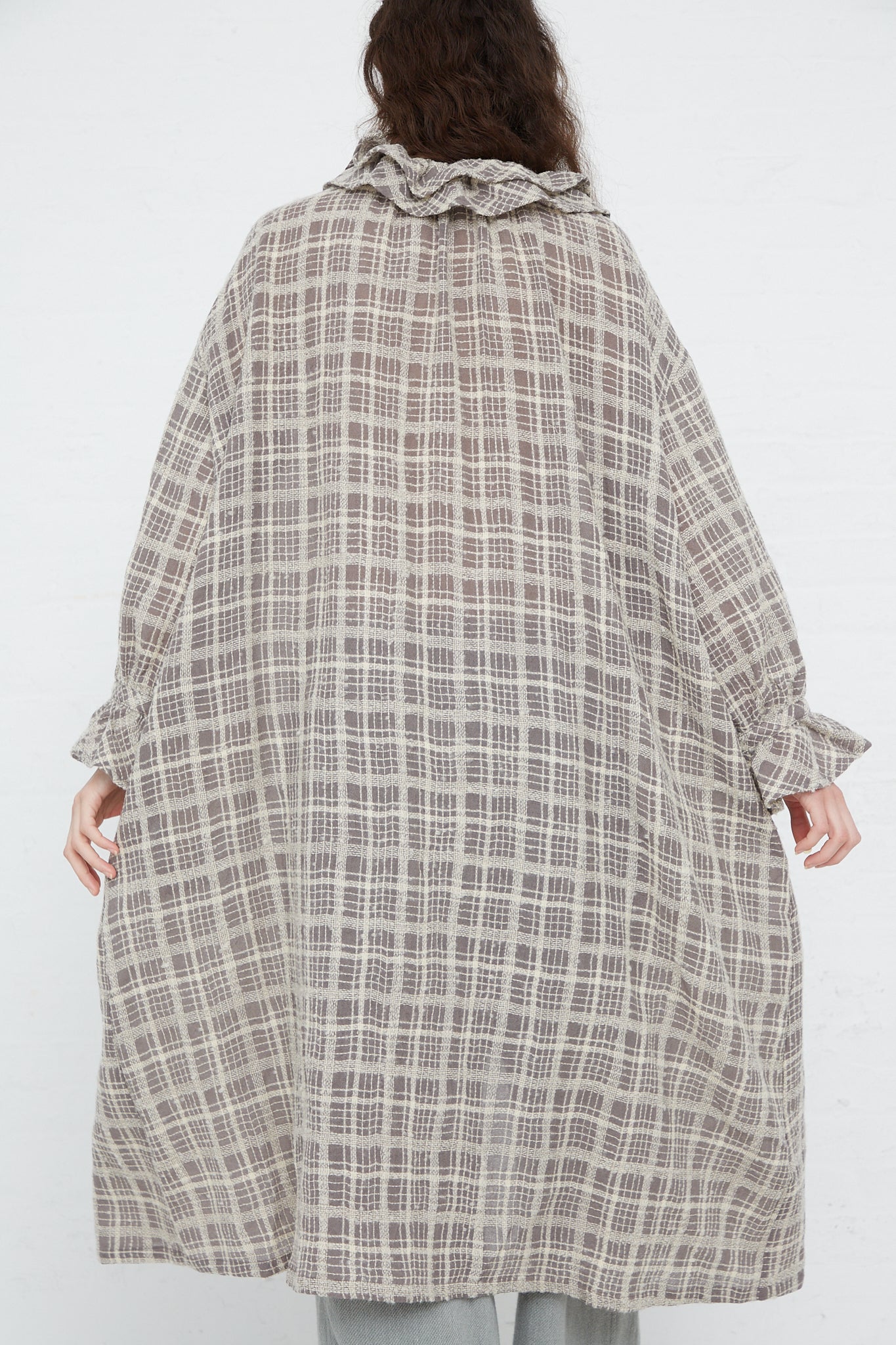 The woman, dressed in a Wool Check Frill Dress in Mocha by Ichi Antiquités, is seen from behind.