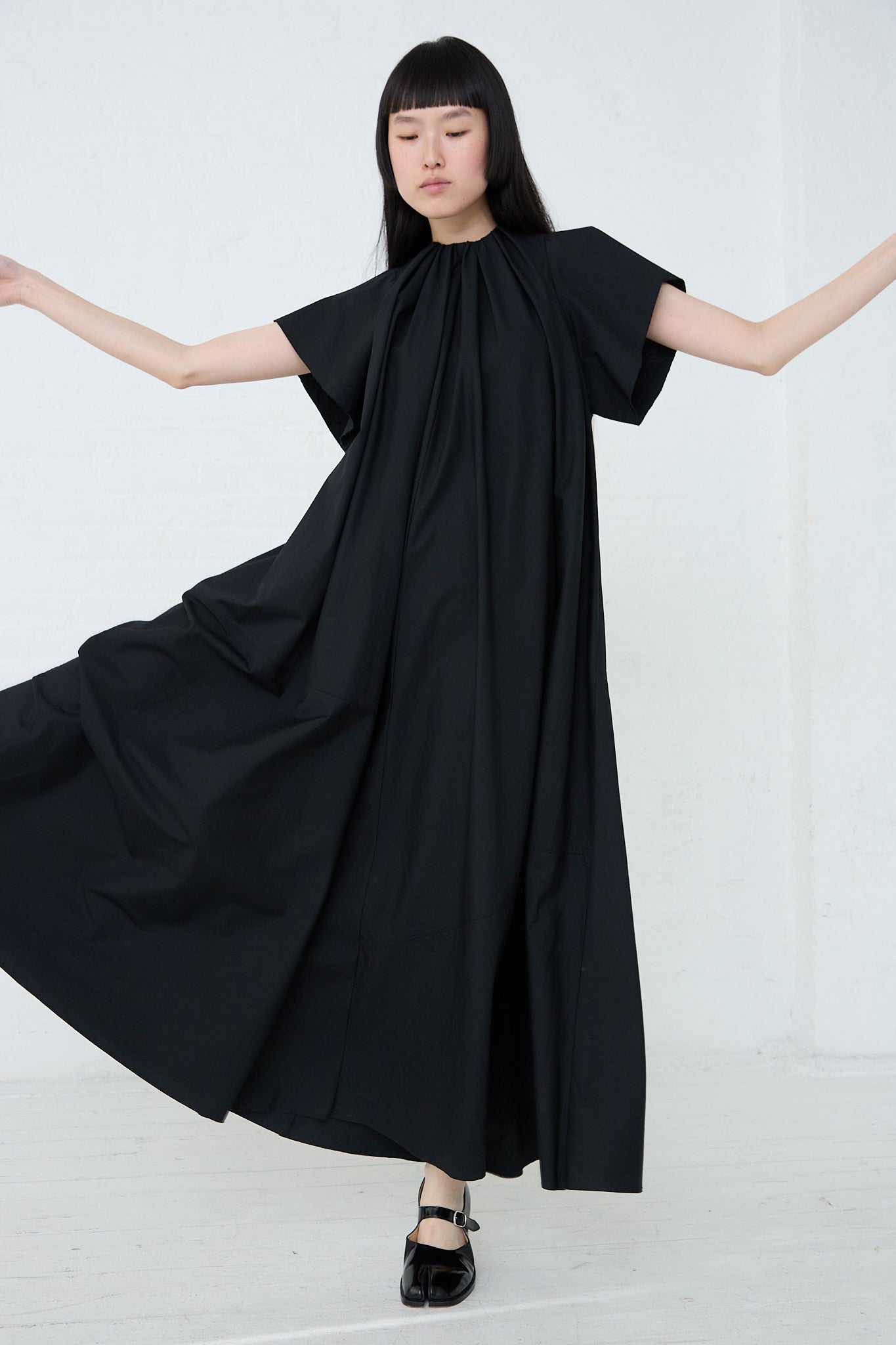 A woman wearing an oversized fit black MM6 maxi dress with long sleeves. Full length. Model dancing.