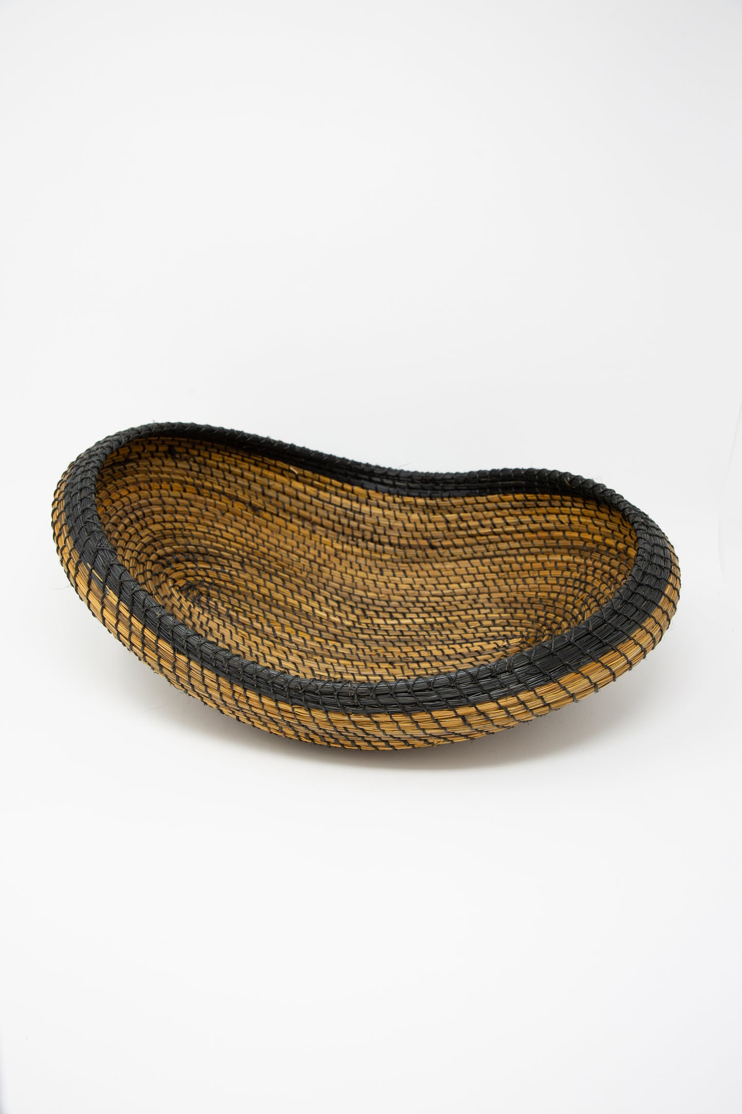 A black and brown Asopafit Canoe Basket, showcasing traditional weaving skills from Colombia by Plaza Bolivar, set against a fresh white background.