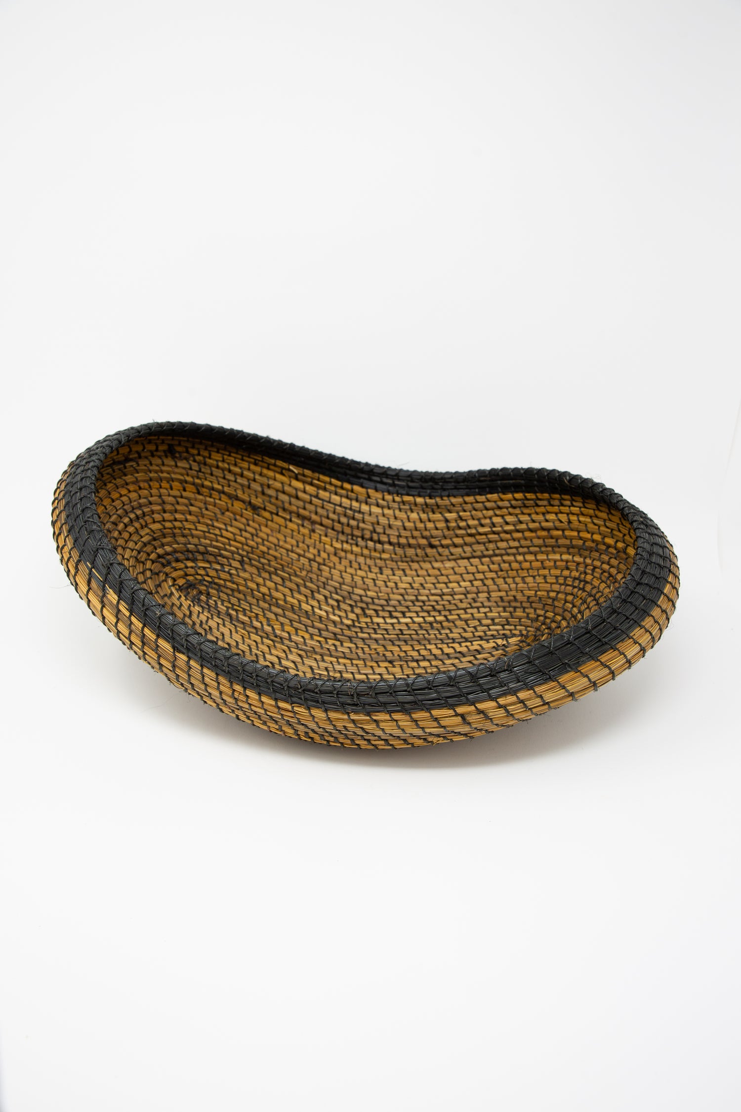 A black and brown Asopafit Canoe Basket, showcasing traditional weaving skills from Colombia by Plaza Bolivar, set against a fresh white background.