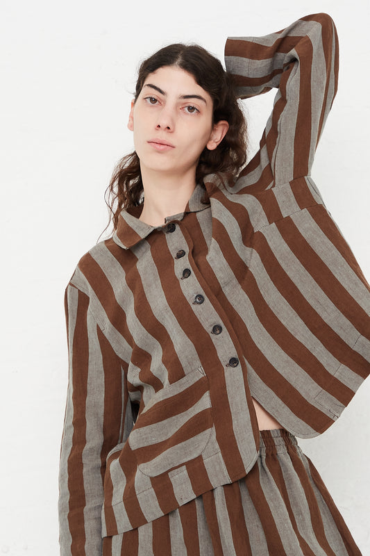A model wearing a lightweight jacket in a striped linen. Features a fold-over collar and a 5-button placket. Front view and upclose. Model has one armed raise to highlight details. Designed by Cawley - Oroboro Store