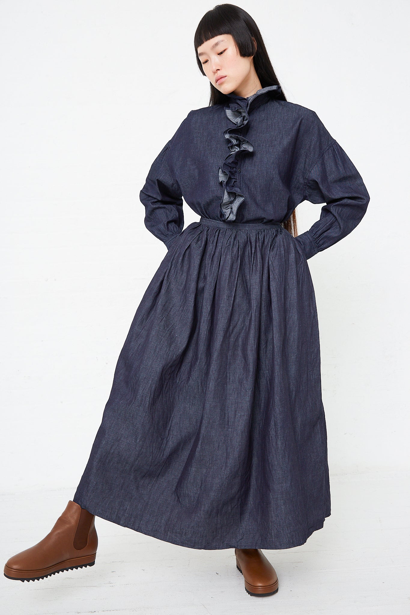A woman wearing a Toujours Cotton Denim Cloth Pleated Maxi Skirt in Indigo and boots.