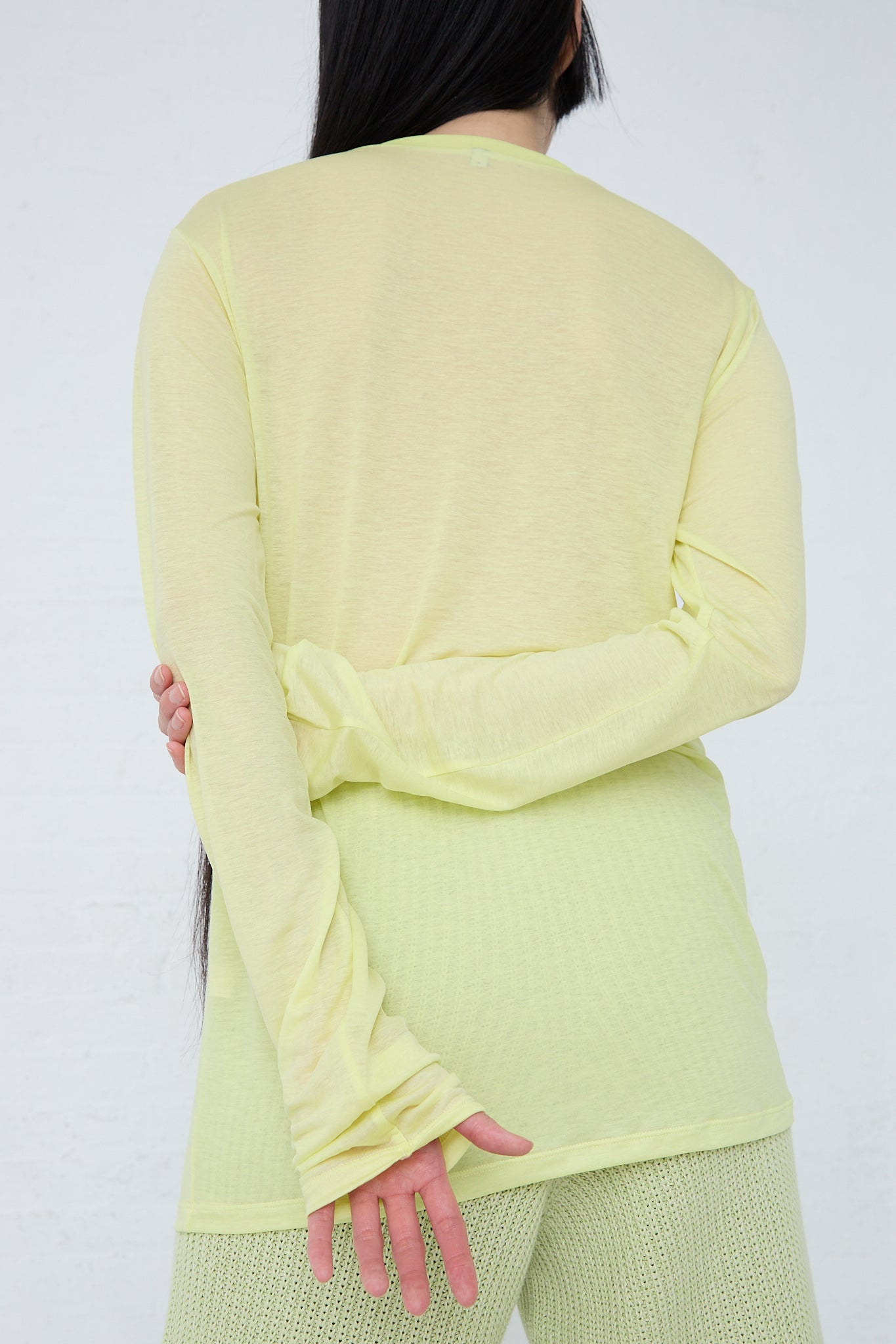 The back view of a woman wearing a Baserange Bamboo Long Sleeve Tee in Lime.