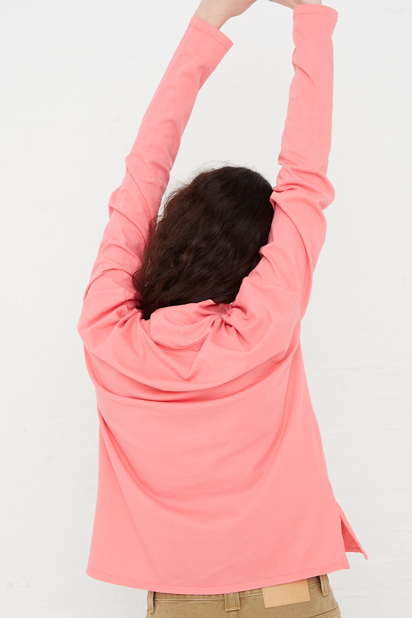 A model wearing a B Sides Cotton Turtleneck Shirt in Calla Pink with her arms outstretched.