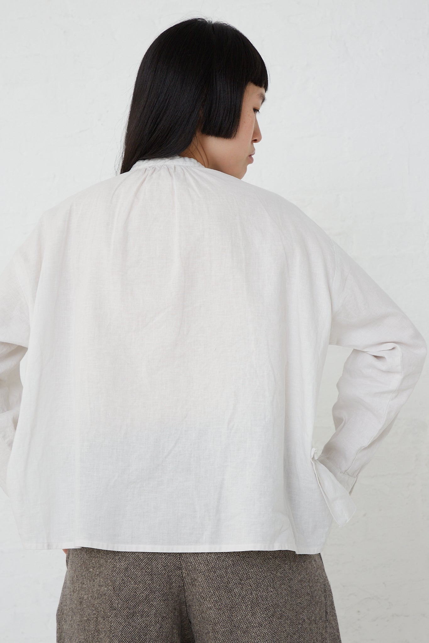 The back view of a woman wearing an UpcycleLino Linen Gathered Frill Blouse in Off White by nest Robe with a front button closure.