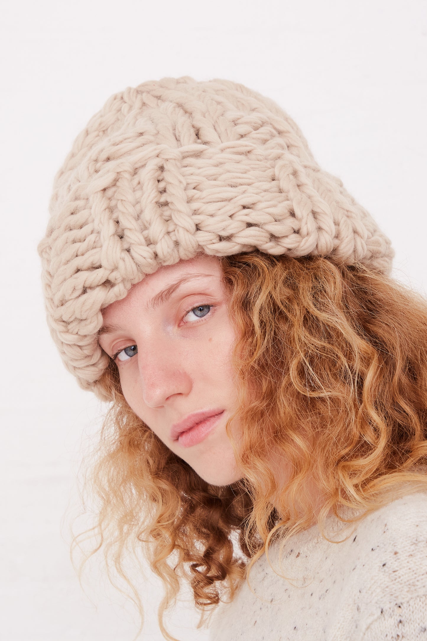 A woman up close wearing an oversized Lauren Manoogian Handknit Chunky Rib Hat in Antique.