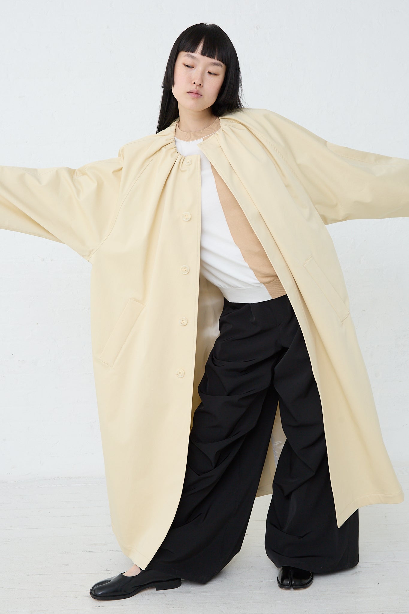 A woman wearing an MM6 Trench Coat in Pale Yellow made of pale yellow cotton twill.