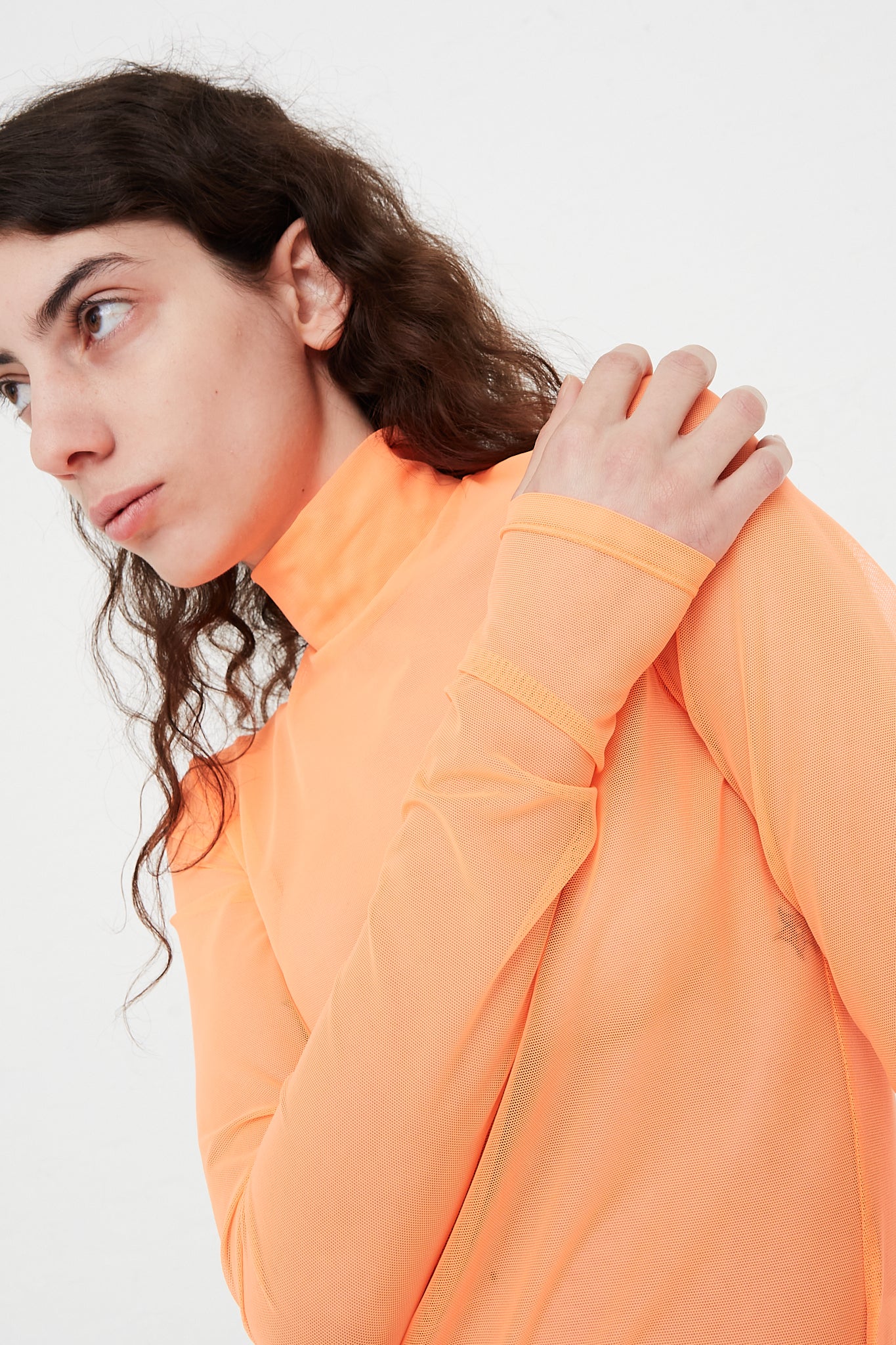 A model wearing a Long Sleeve Mesh Mockneck in Fluoro Orange at Oroboro Store designed by Nomia brand.