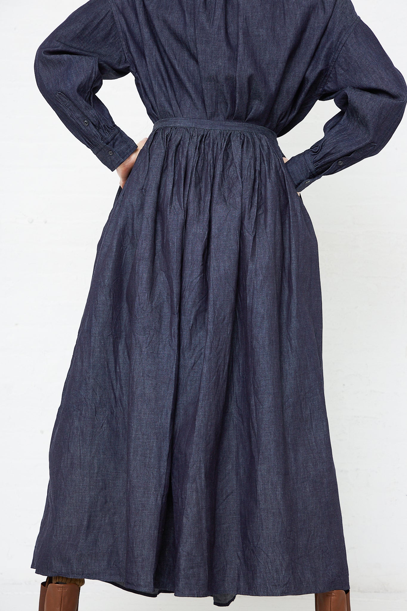 The back view of a woman wearing a Toujours Cotton Denim Cloth Pleated Maxi Skirt in Indigo dress.