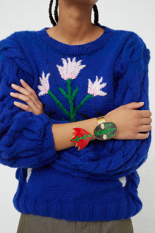 A woman wearing a blue Sofio Gongli sweater with enamel flowers on it.