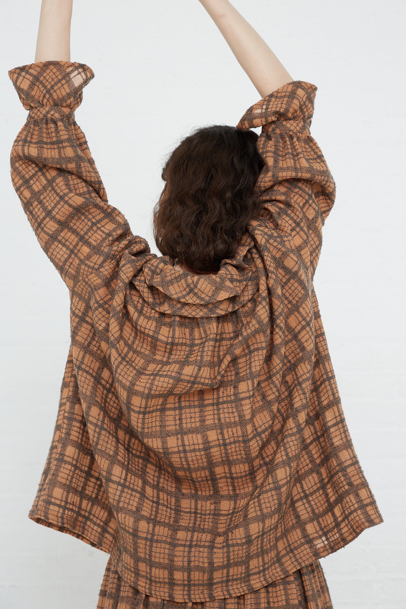 A woman in a relaxed fit Wool Check Frill Blouse in Terracotta by Ichi Antiquités, with her arms up.