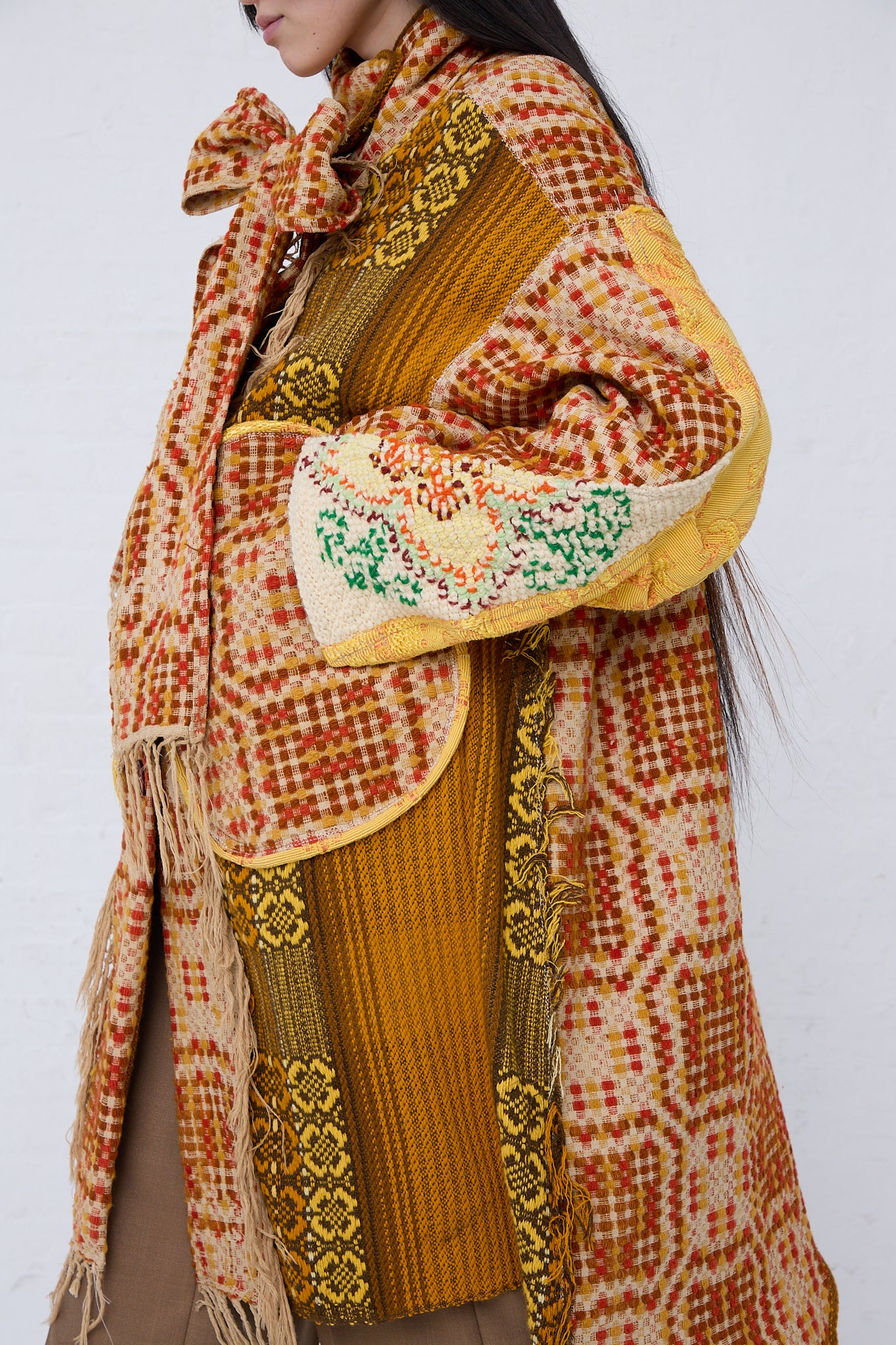 A woman wearing a Thank You Have A Good Day Patchwork Blanket Scarf Parka in Red, Yellow and Brown. Side view with hand in pocket.