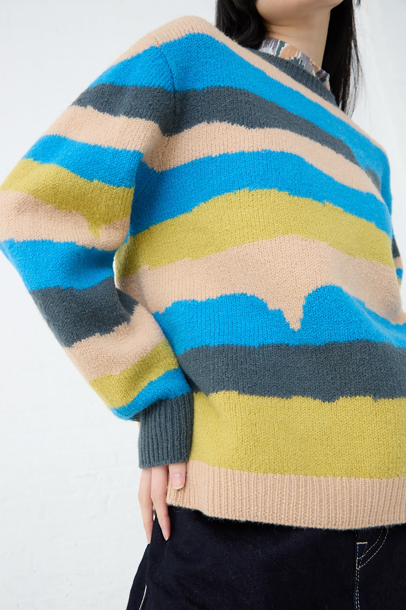 A woman wearing a vibrant striped Light Wind Sweater in Blue Mix, made with alpaca/wool blend by Mina Perhonen. Front view and up close.