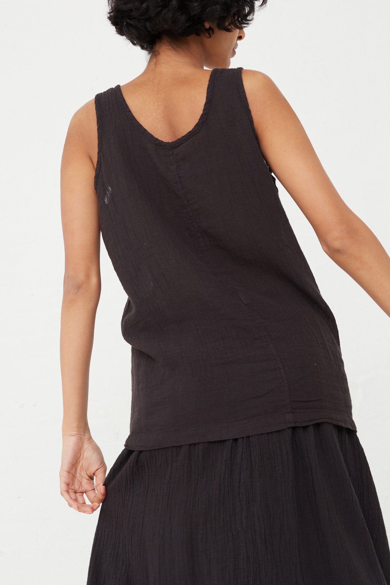 The Black Crane Tank Top in Black, made of a cotton linen blend, showcasing the back view of woman.