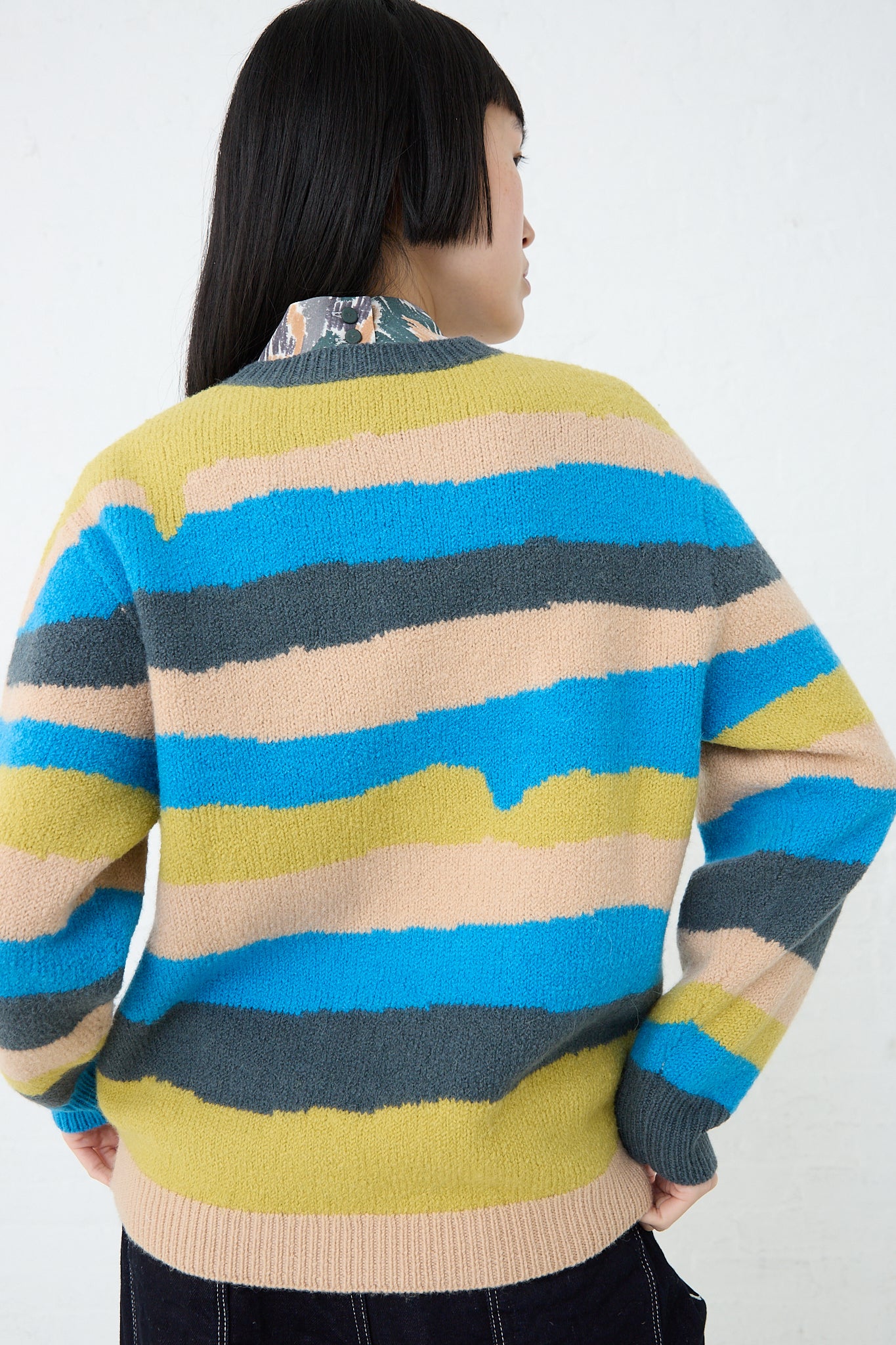 The back view of a woman wearing a Mina Perhonen Light Wind Sweater in Blue Mix.