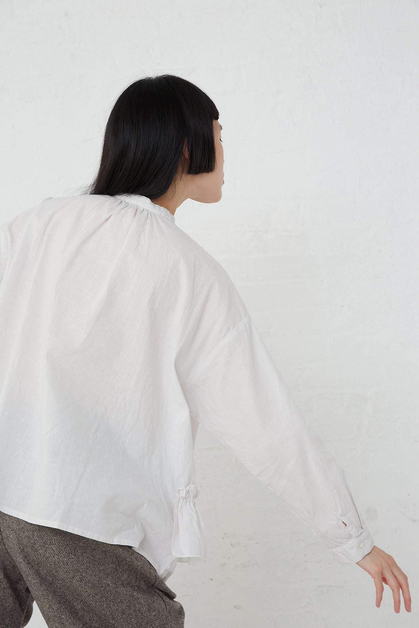 A woman wearing a nest Robe UpcycleLino Linen Gathered Frill Blouse in Off White with front button closure and trousers.