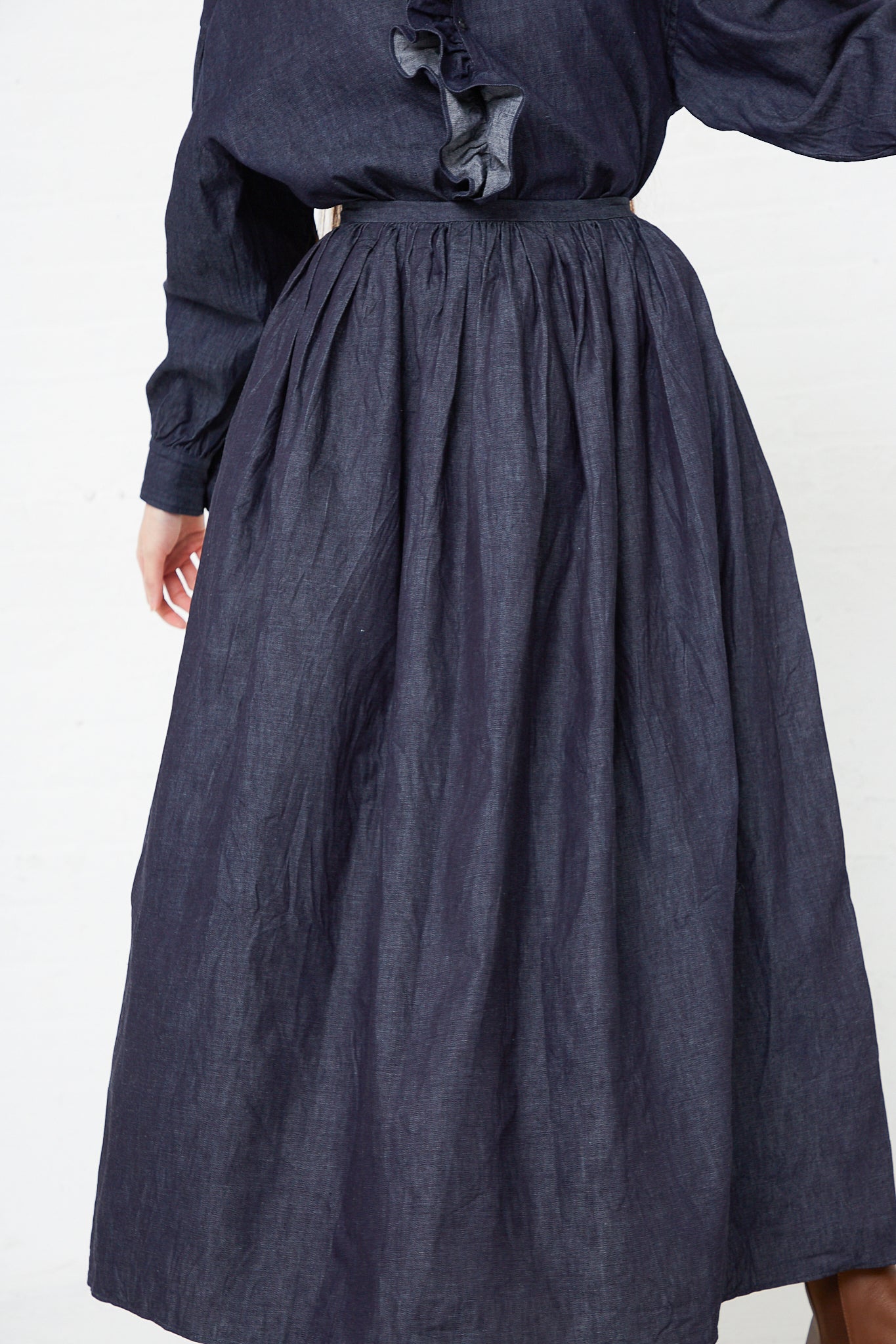 A woman wearing a Toujours Cotton Denim Cloth Pleated Maxi Skirt in Indigo.