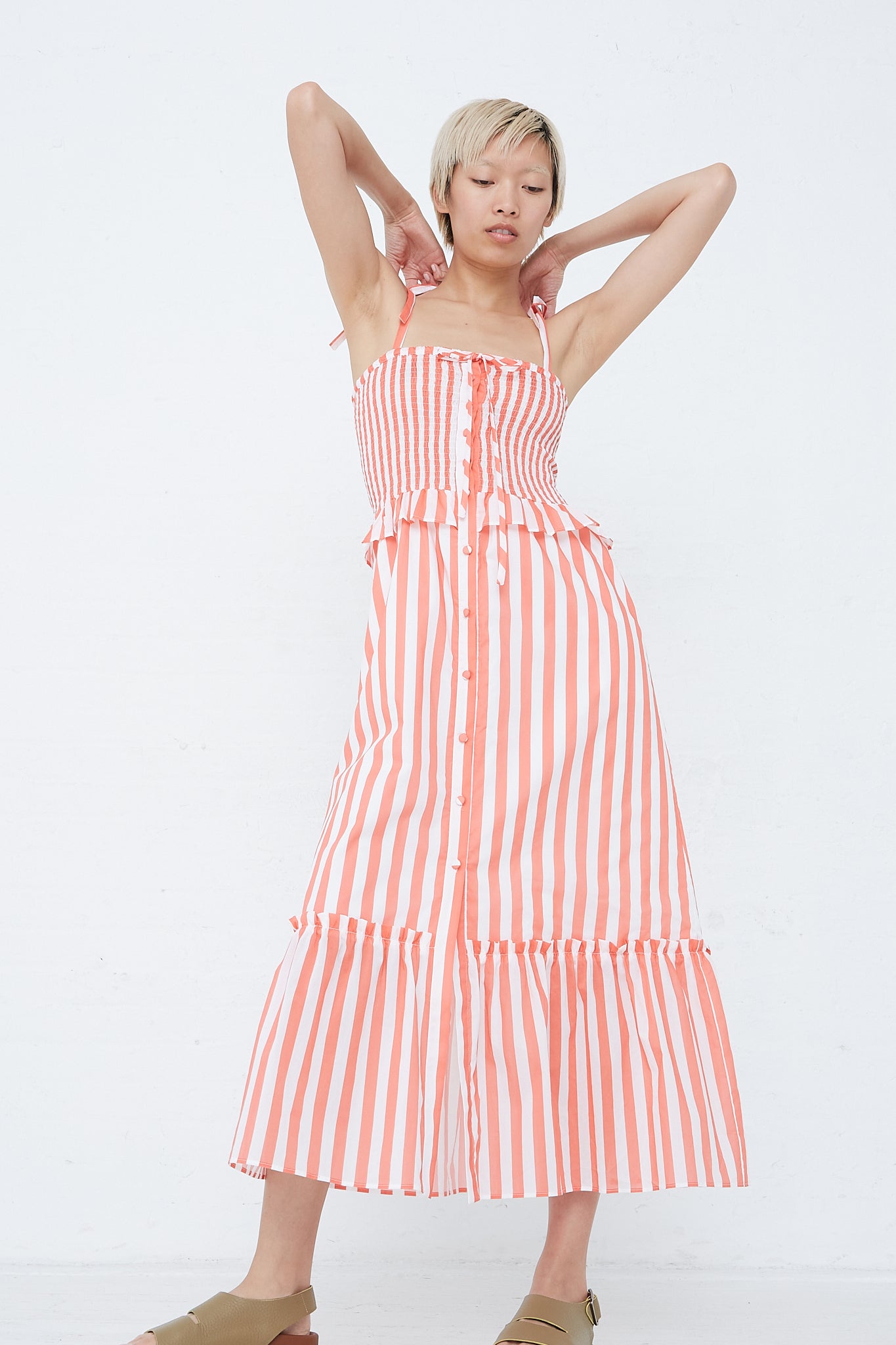 A woman in the Loretta Caponi Alberica Dress in Coral Stripe with adjustable tie straps.