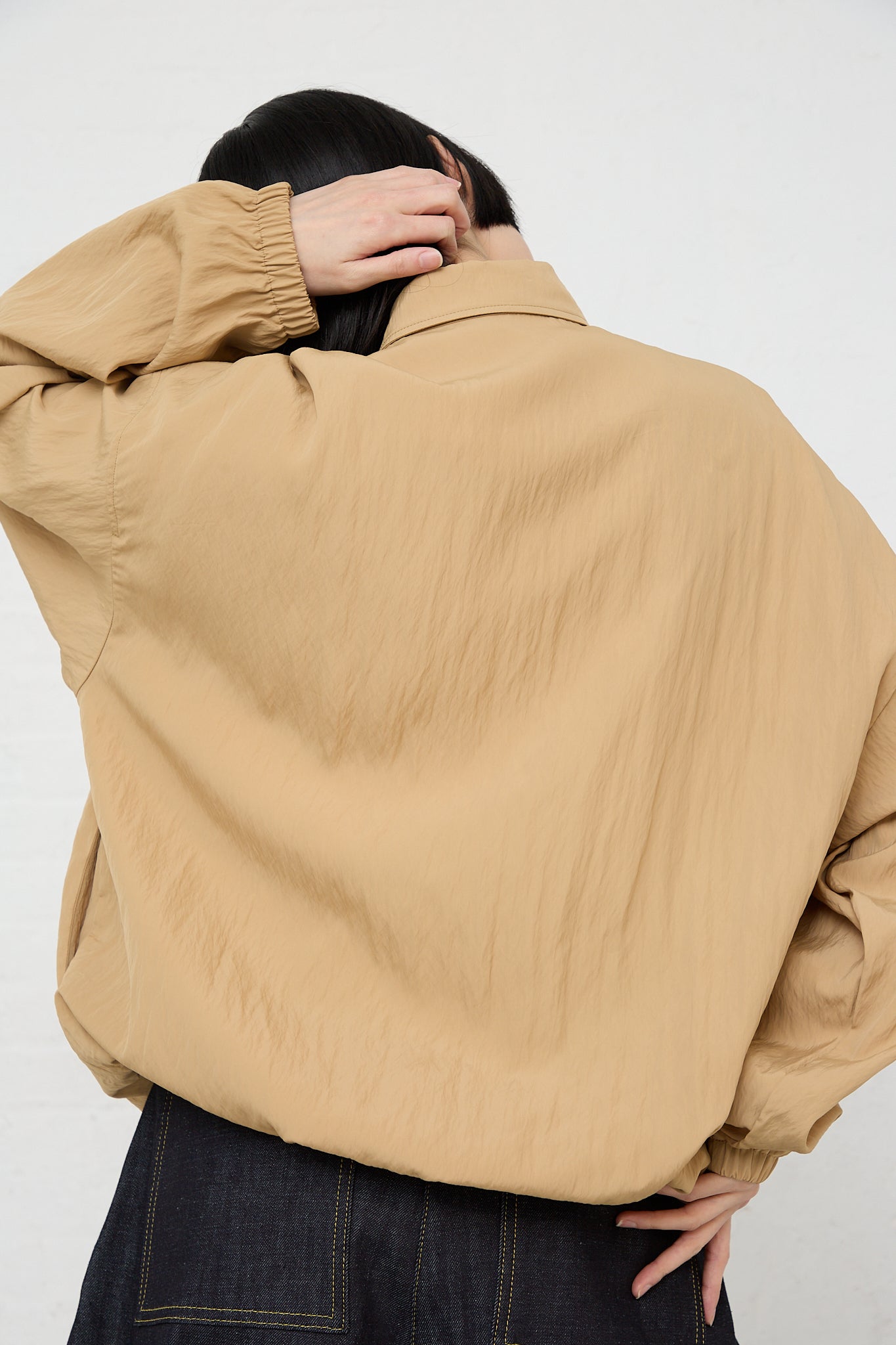 A woman wearing a Studio Nicholson Sprung Coach Jacket in Sand with elasticated cuffs.