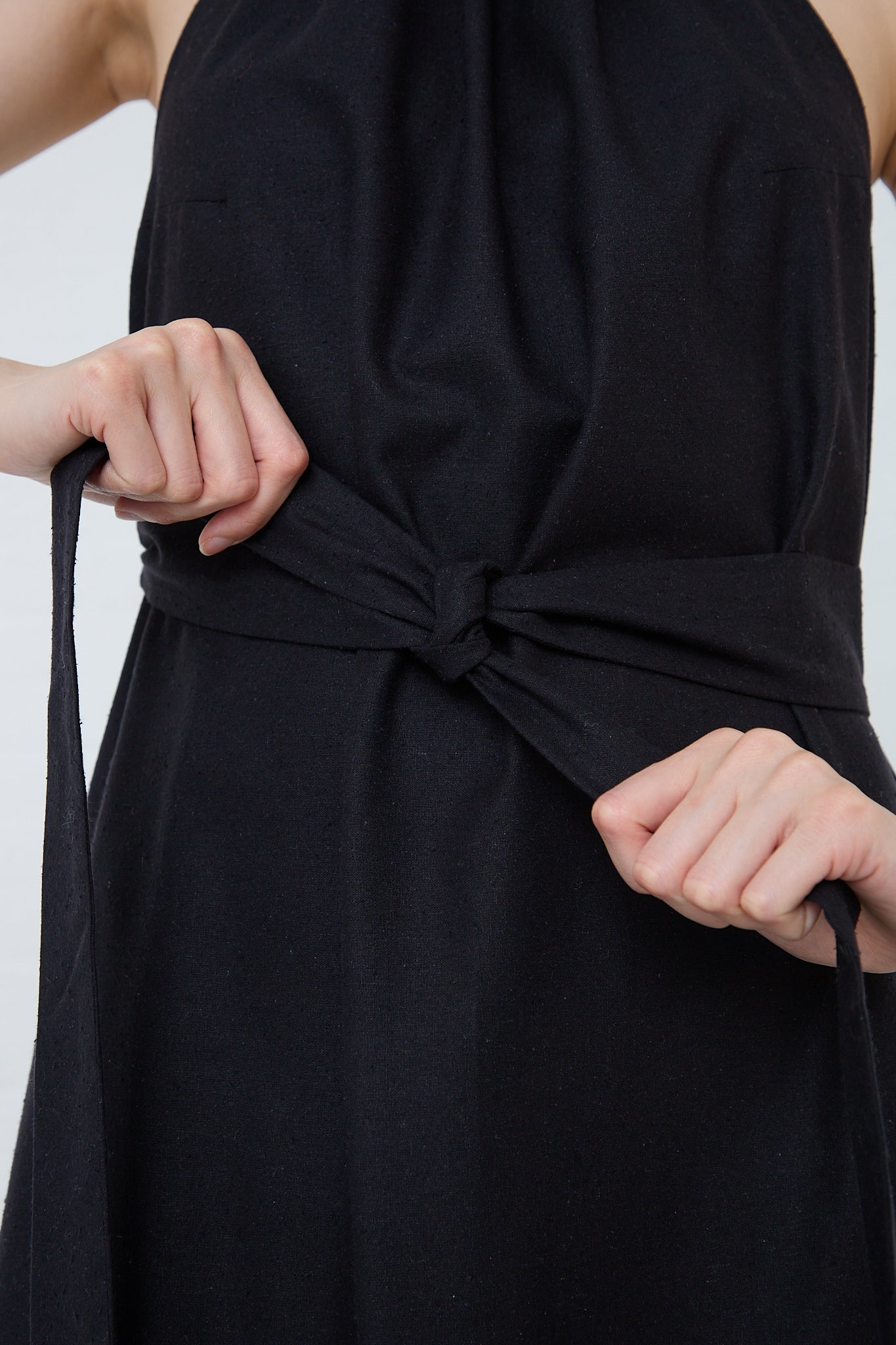 A woman wearing a Wild Silk Trope Apron Dress in Black with a belt, crafted from exquisite black wild silk, by Baserange. Up close view of wrap belt.