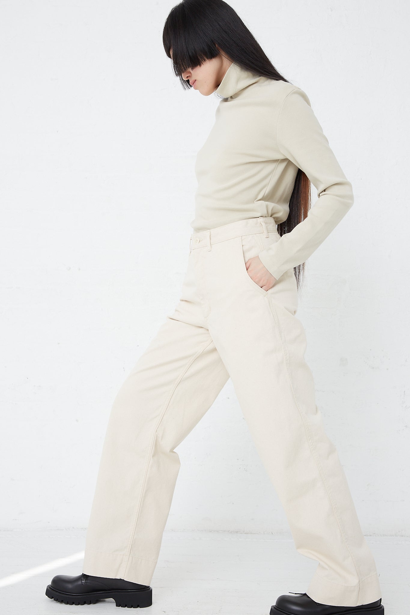 A woman wearing a turtle neck and wide leg pants in As Ever's 51 Chino in Natural.