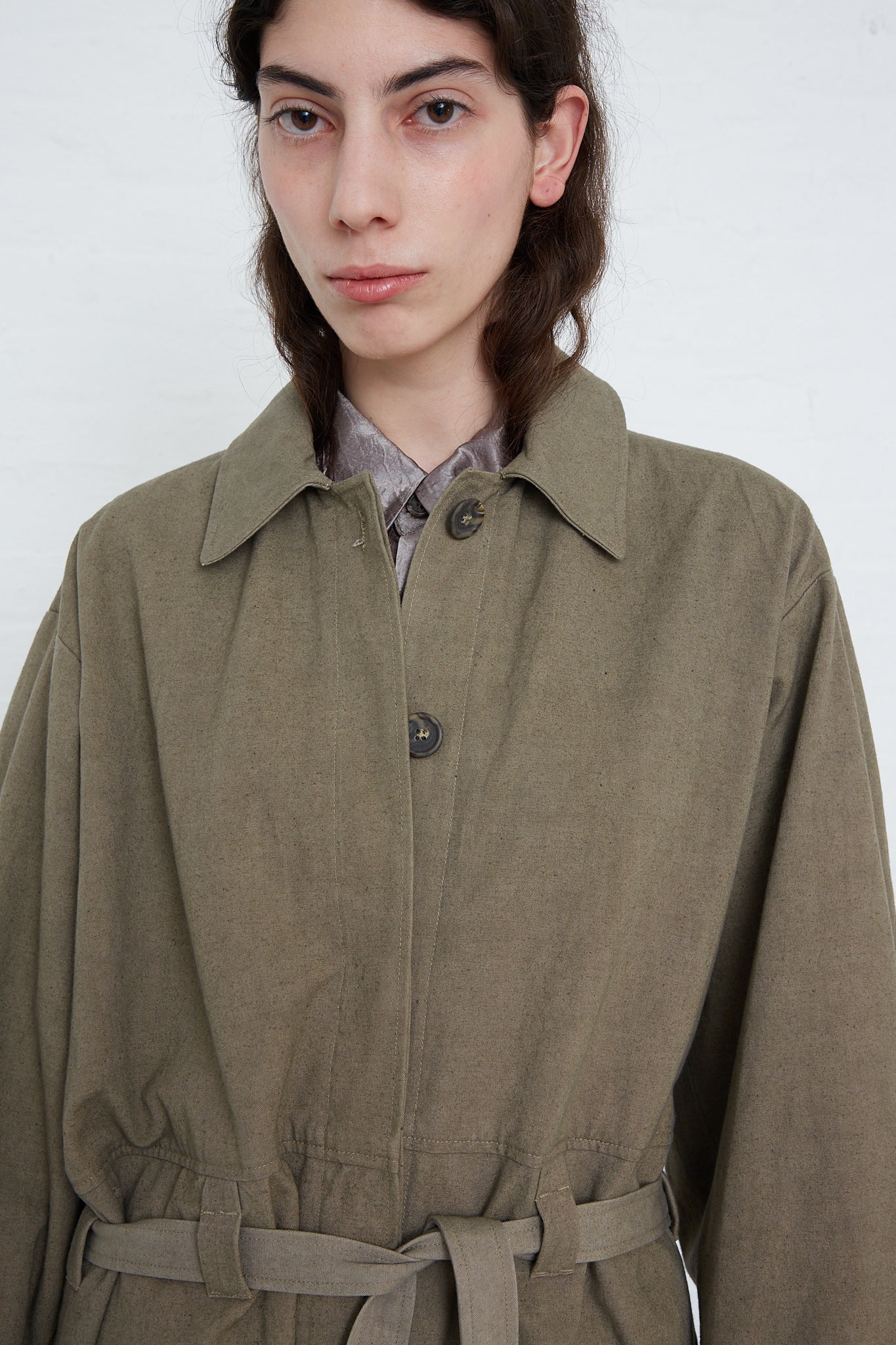 A woman wearing an oversized beltred trench in fatigue with adjustable cuffs by Lauren Manoogian.
