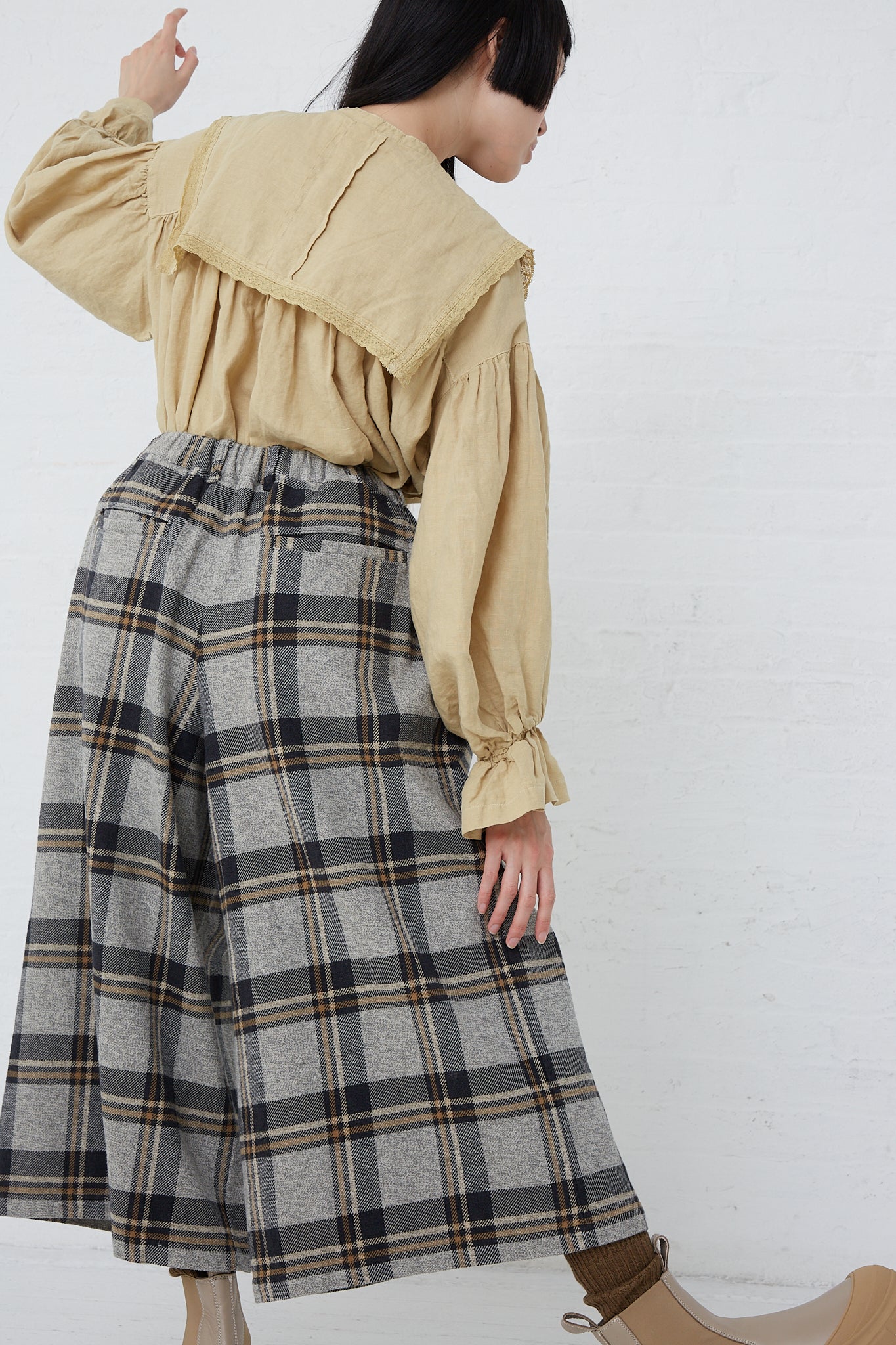 A woman wearing a nest Robe Cotton Heavy Twill Plaid Wide Leg Pant in Navy and boots. Back view.