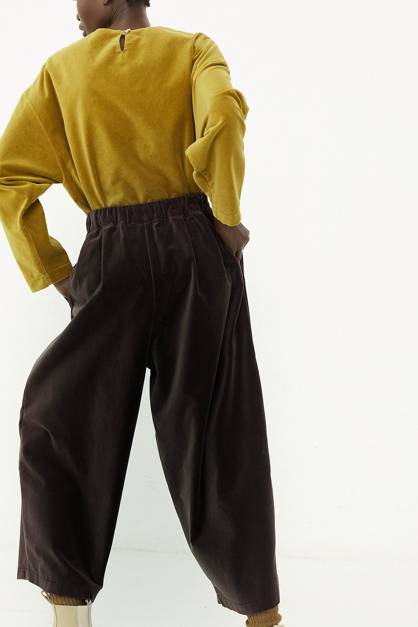 A woman in a yellow shirt with wide leg pants is standing in front of a white background wearing Black Crane's Cotton Velveteen Wide Pants in Sumi Black.